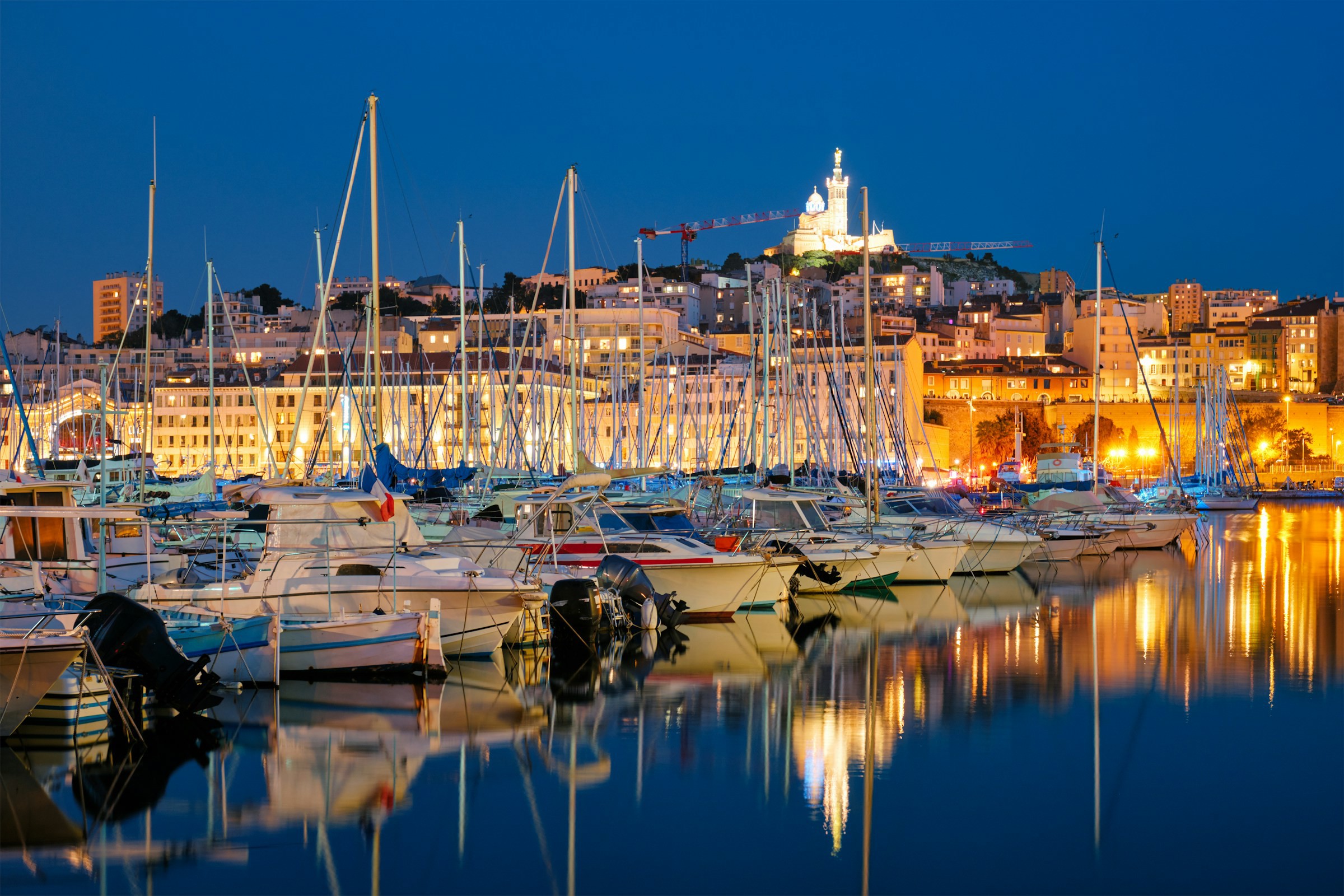 Boats in a harbor during the evening with an illuminated city in the background