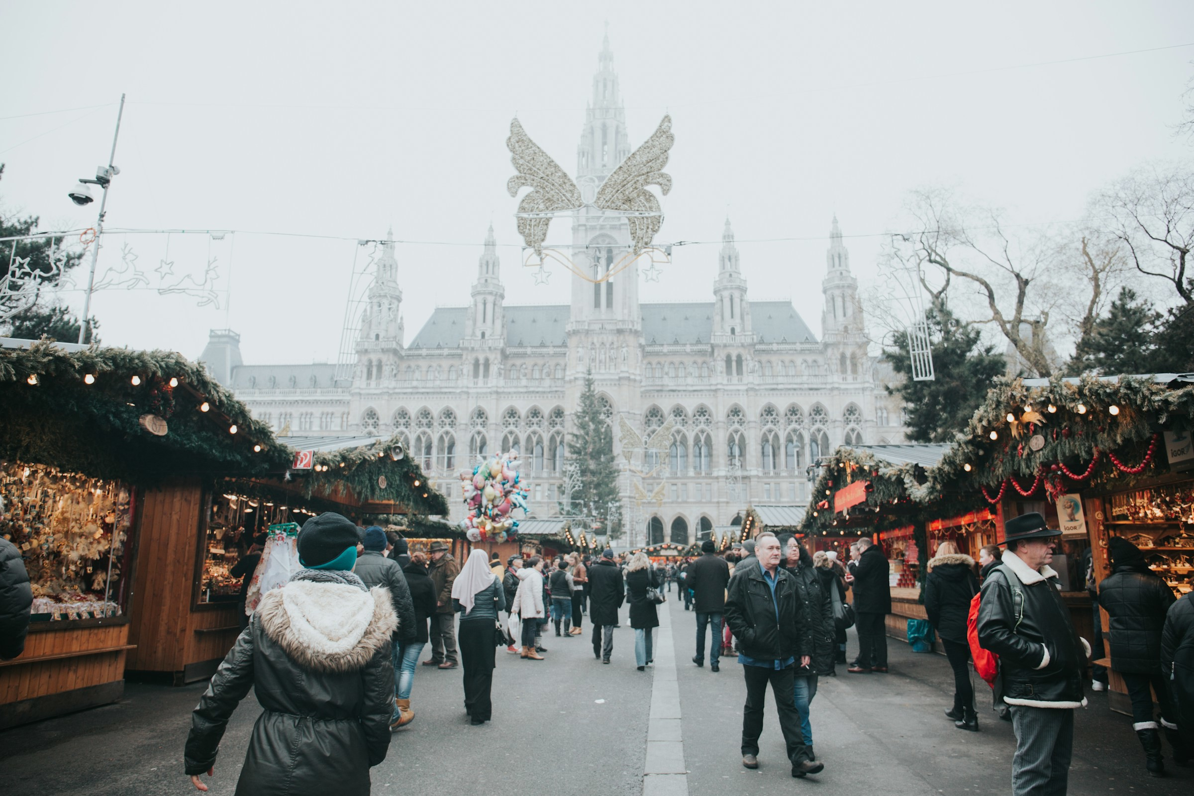 Julmarknad med besökare framför historisk byggnad dekorerad med en stor ängel på en kall vinterdag i Wien, Österrike.