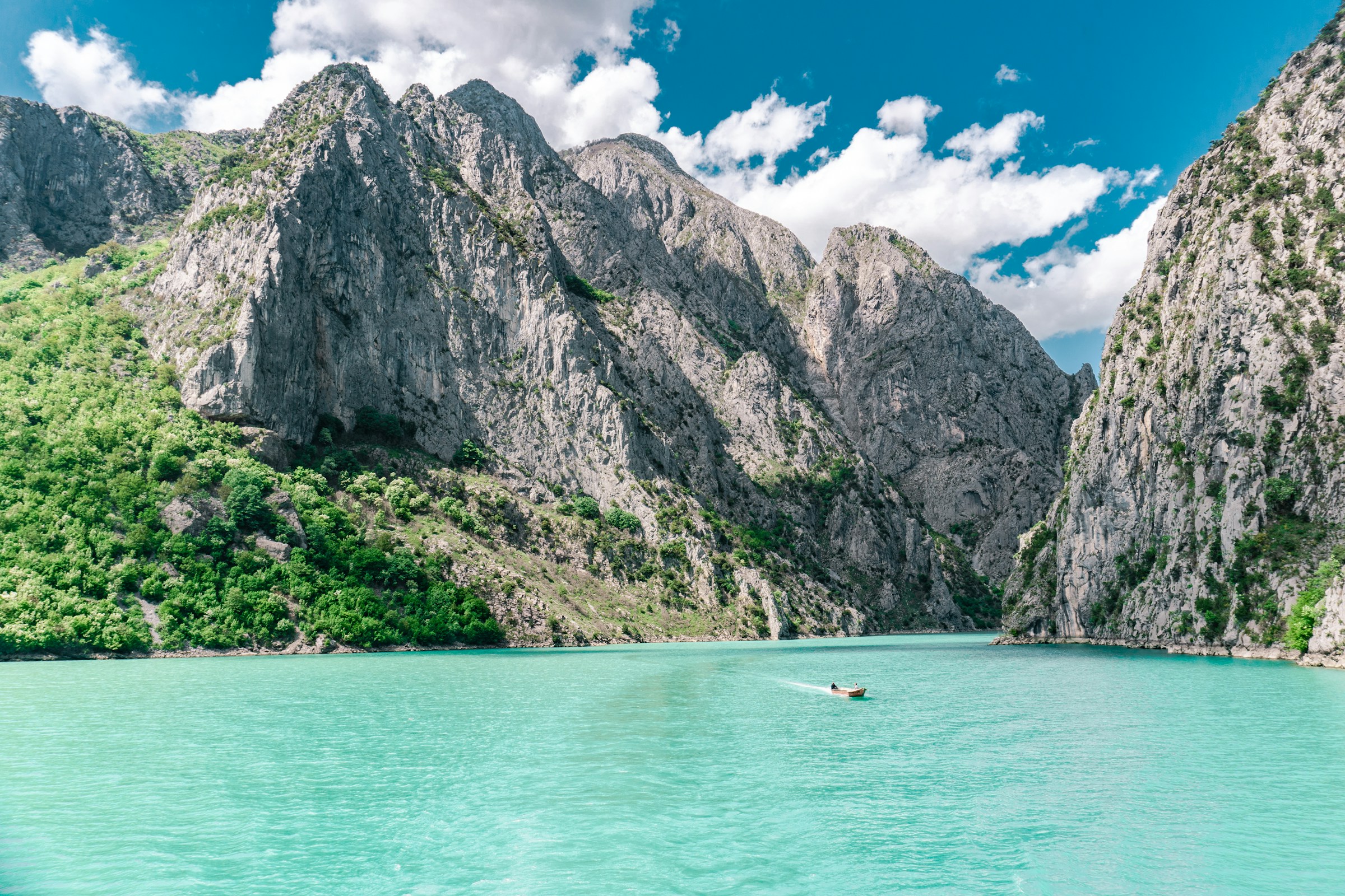 Turkos sjö omgiven av branta klippiga berg och en liten båt som flyter på vattnet i Albanien.