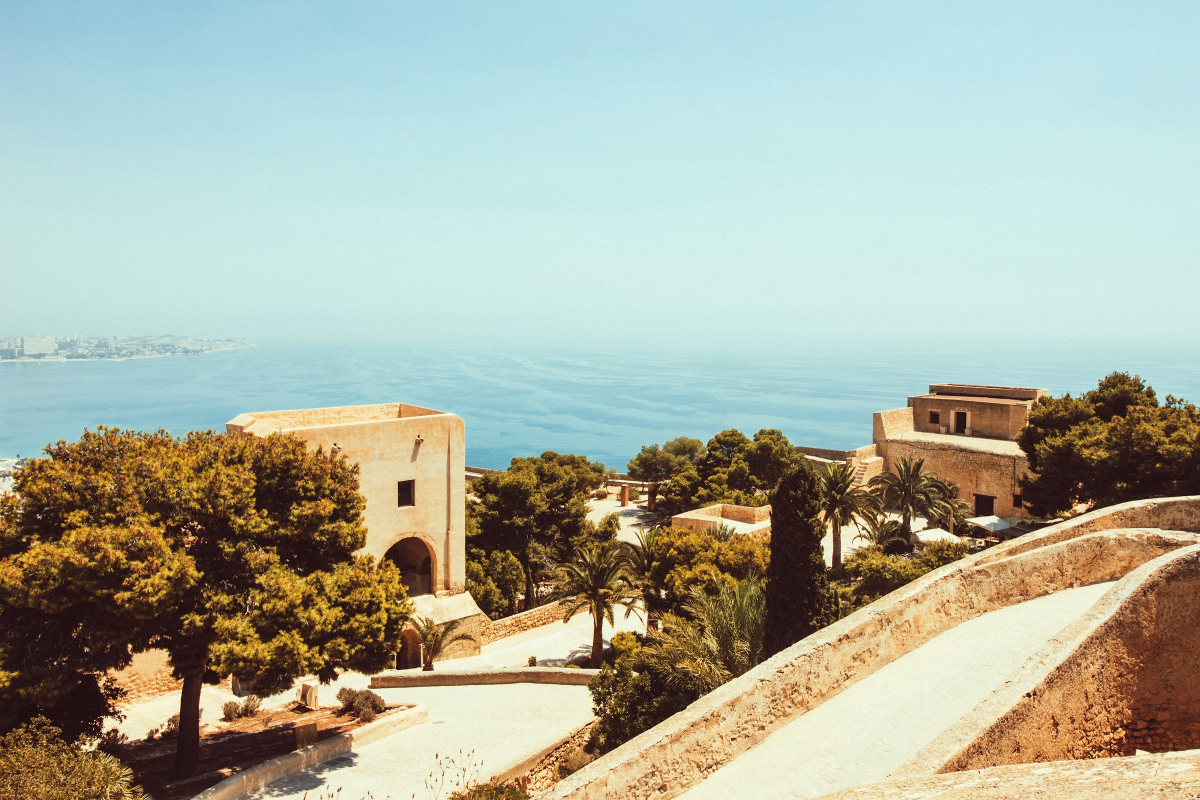 Panoramautsikt över medelhavsstaden med traditionella byggnader och gröna träd mot en blå himmel och hav i bakgrunden i Malaga.