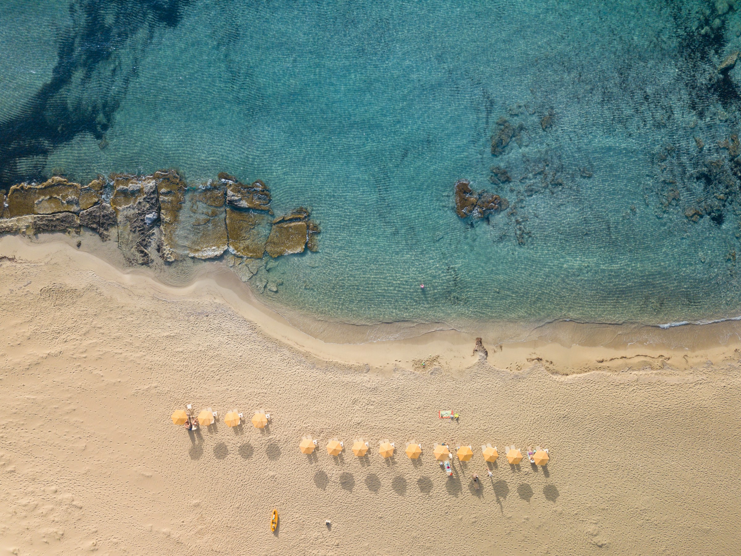 Flygfoto över solstolar och parasoller på en sandstrand vid kristallklart hav på Kreta i Grekland