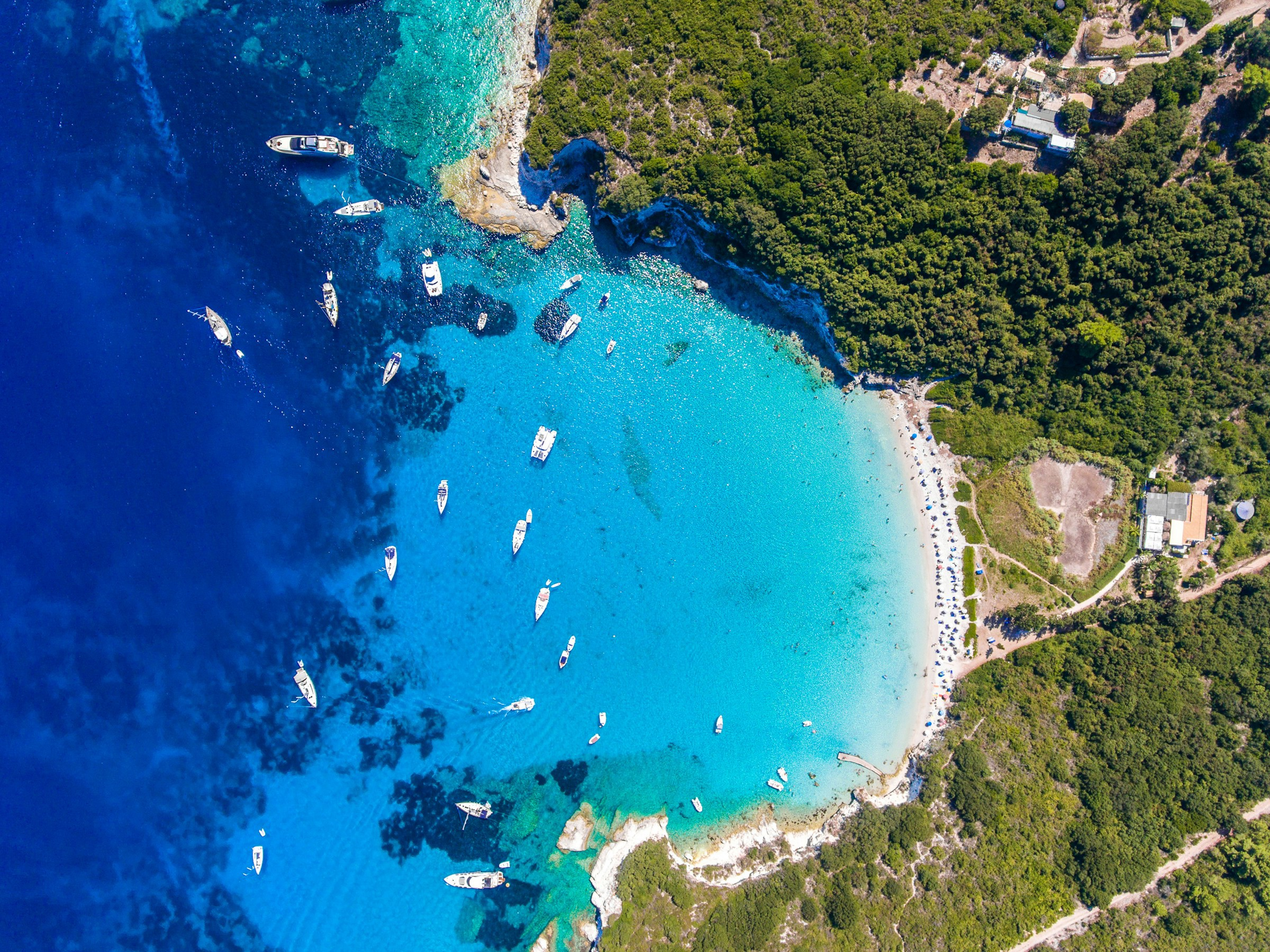 vy ovanifrån över blått hav som möter vit sandstrand på grekiska ön paxos