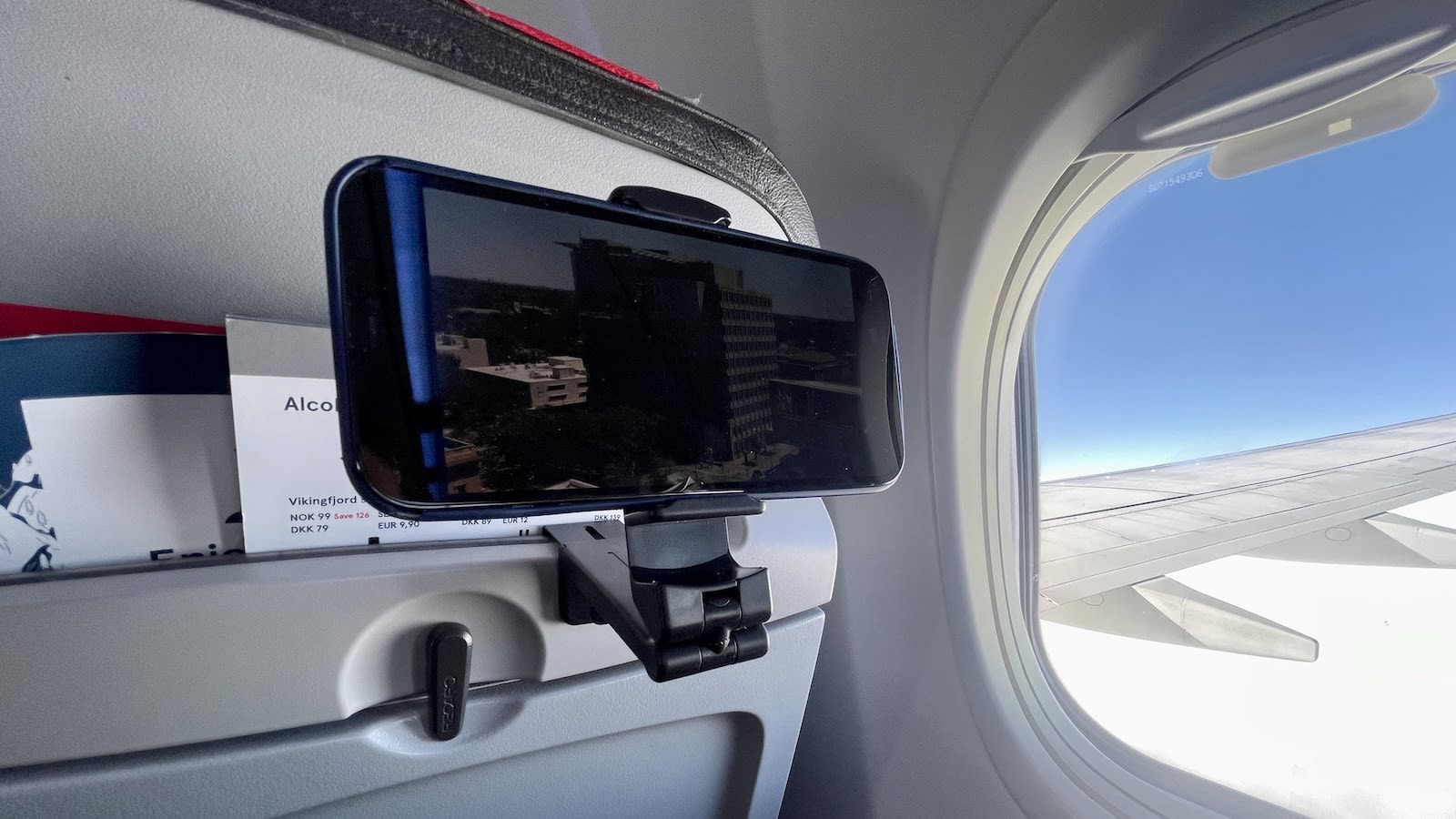 Phone with attachment to the seat of an airplane with window out and blue sky on the side