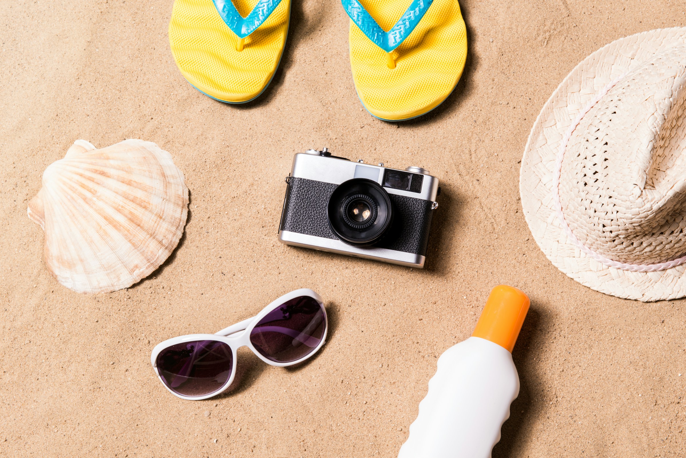 Travel products such as a hat, camera, and sunscreen on a sandy beach