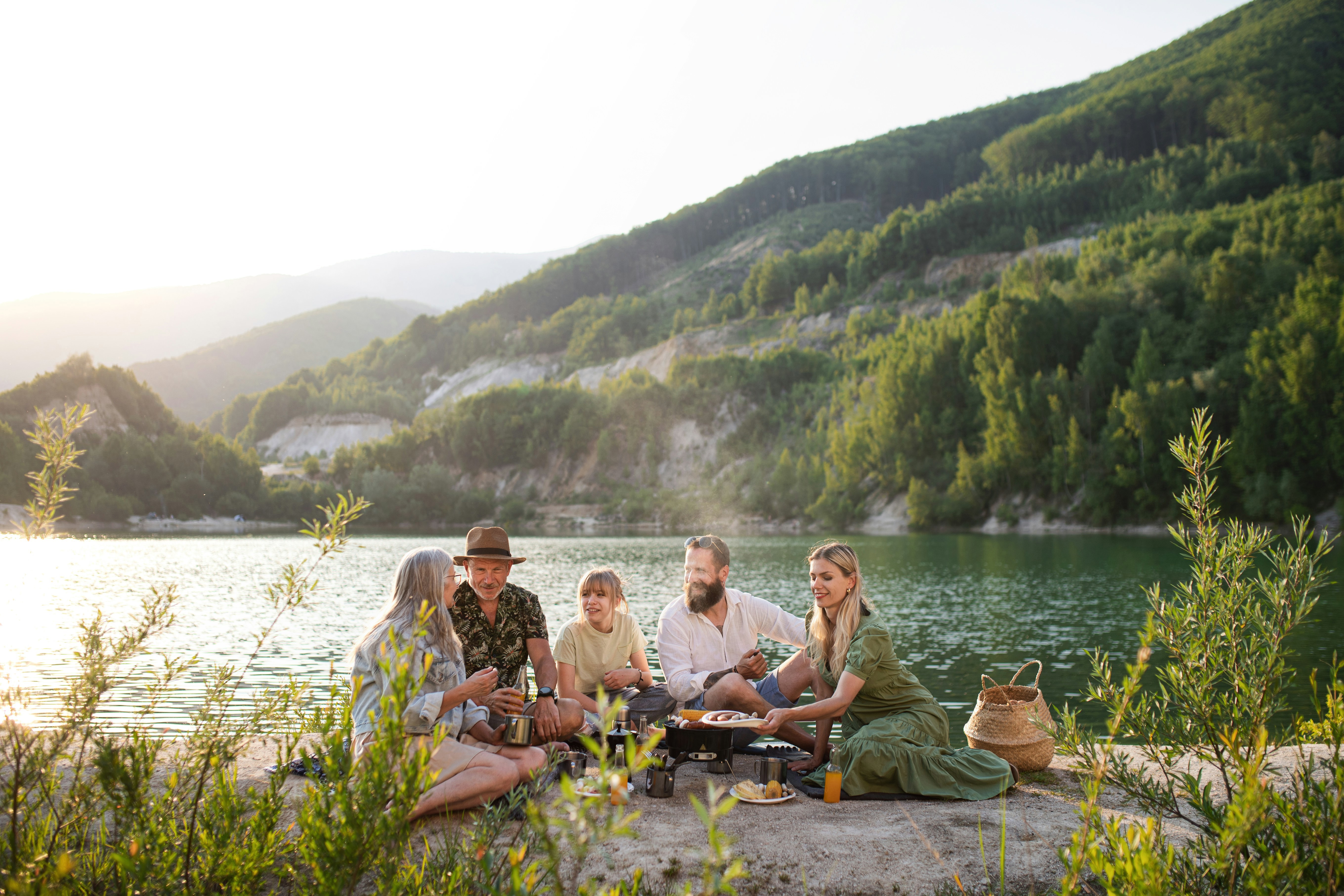 en grupp med vänner sitter vid en sjö och umgås med vackra berg i bakgrunden