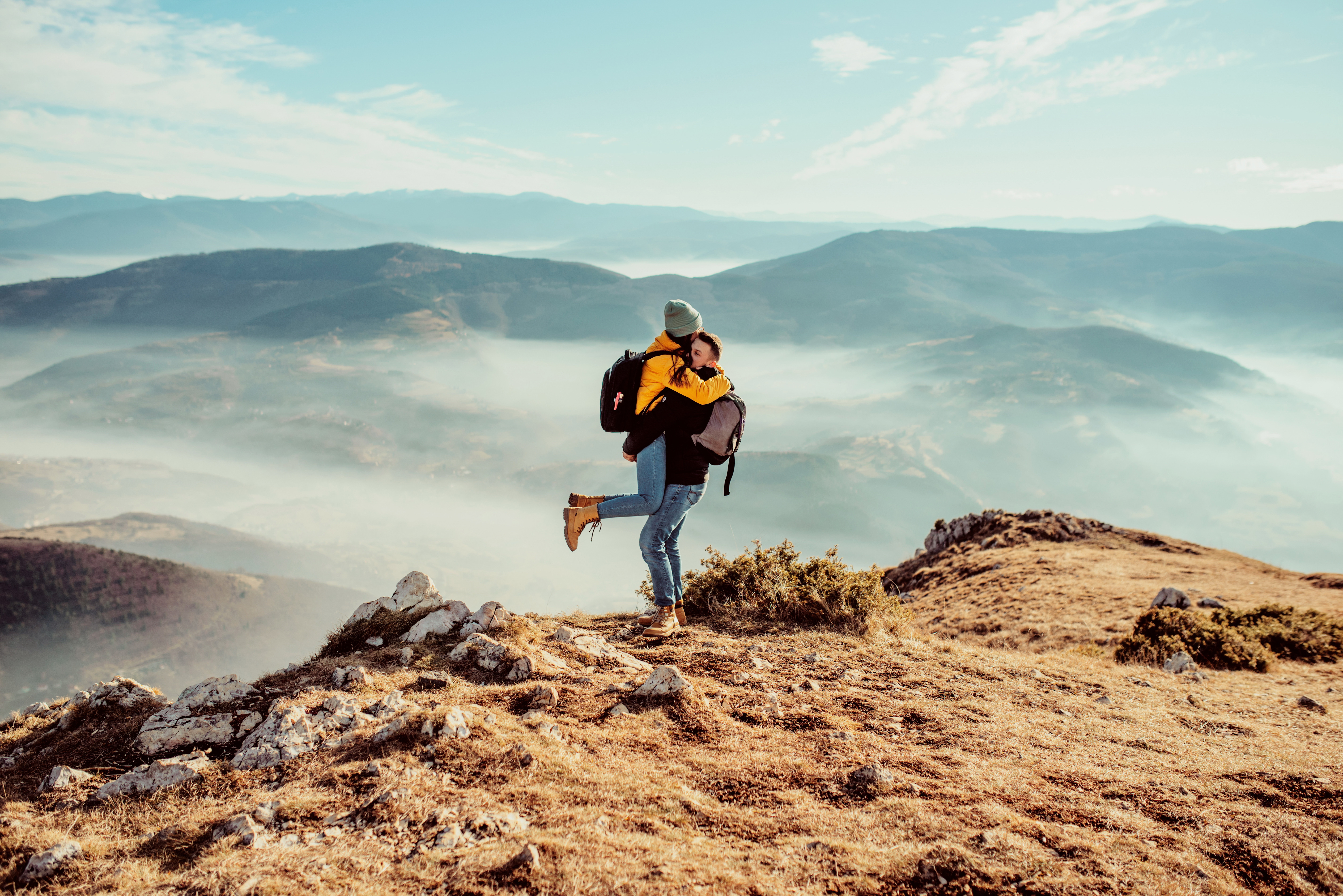 Par är försäkrade på resan och kramas på en bergstopp med dimmiga dalar i bakgrunden.