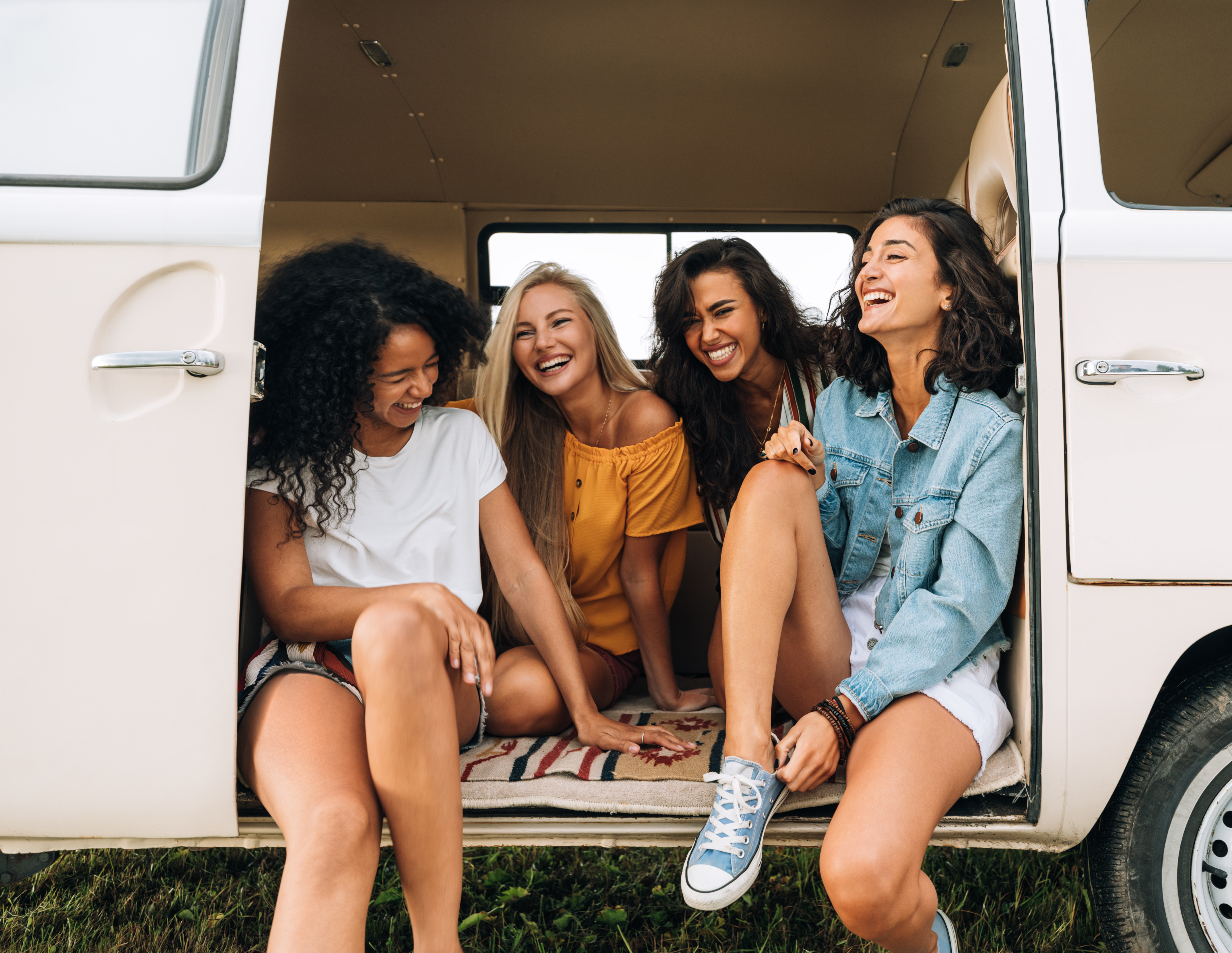 Reseförsäkring för resan - Glada unga kvinnor sitter och skrattar i en skåpbil under en sommardag, vänskap och roadtrip-koncept.
