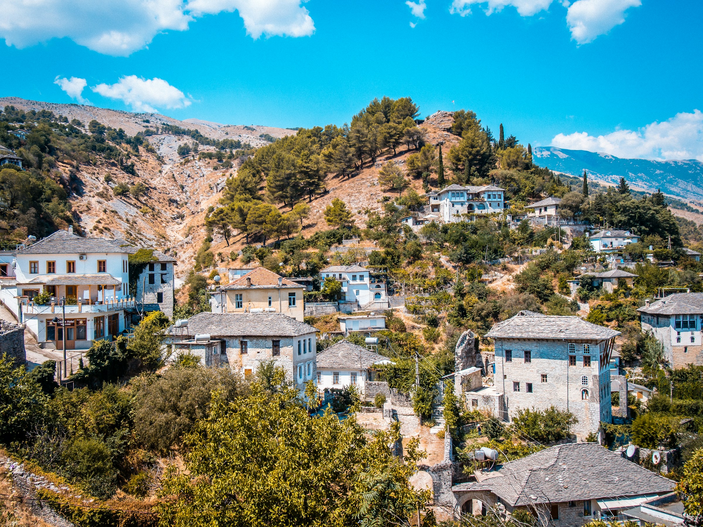 Pittoresk bergsby med traditionella hus och kullerstensgator omgivna av grönskande landskap och blå himmel i Albanien.