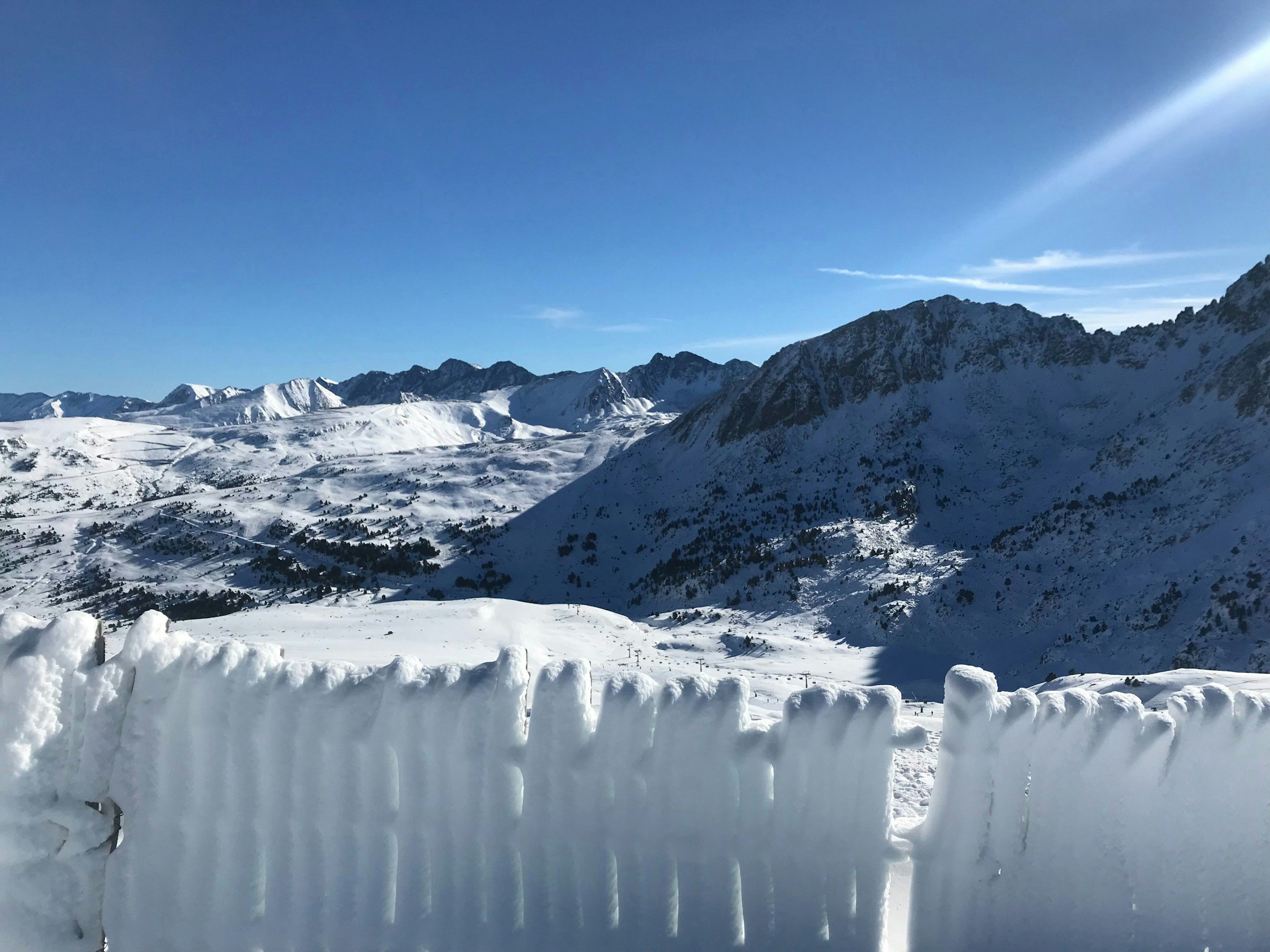 Snow-covered winter landscape leading up to mighty mountains and blue skies in Grandvalira, Andorra