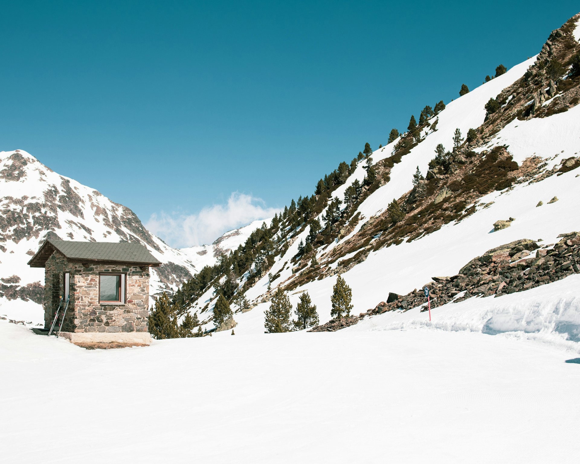 Stenstuga i snöklädda bergslandskap med blå himmel i Andorra.