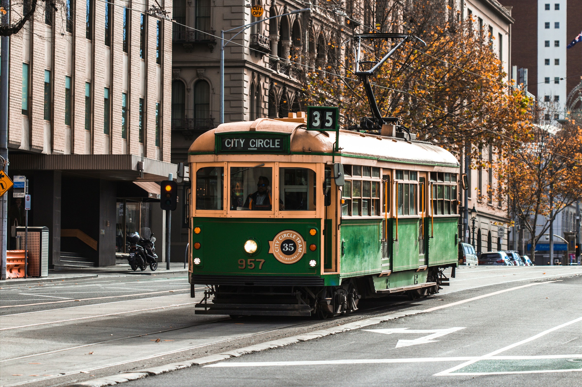 Grön och gul gammaldags spårvagn märkt "City Circle" kör på gata i Melbourne med höstträd och byggnader i bakgrunden.