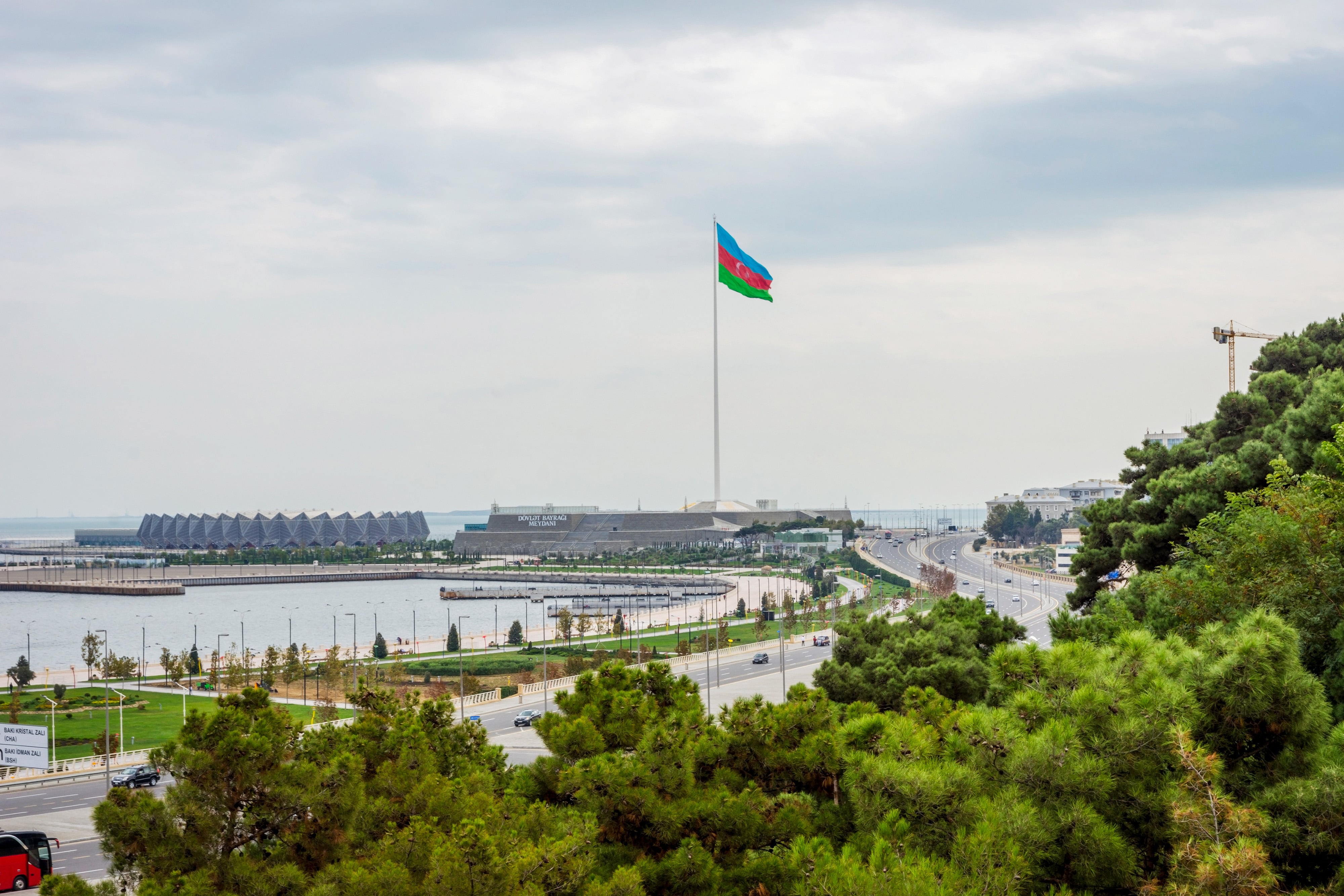 Resa till Azerbajdzjan - Vy över hamn i en stad och hamn med grönska runtomkring med Azerbajdzjans flagga som når en vit himmel