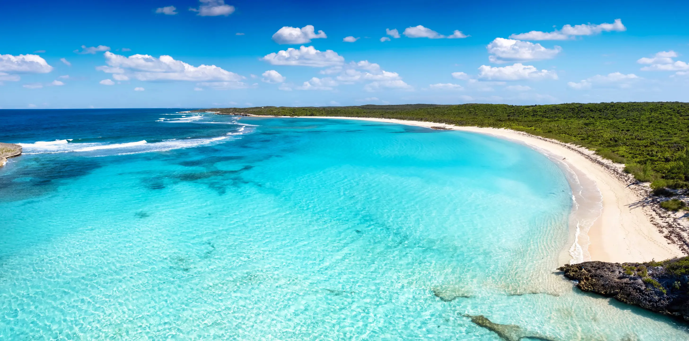 Resa till Bahamas - Flygfoto av en orörd strand med kristallklart blått hav och frodig grönska på en solig dag.