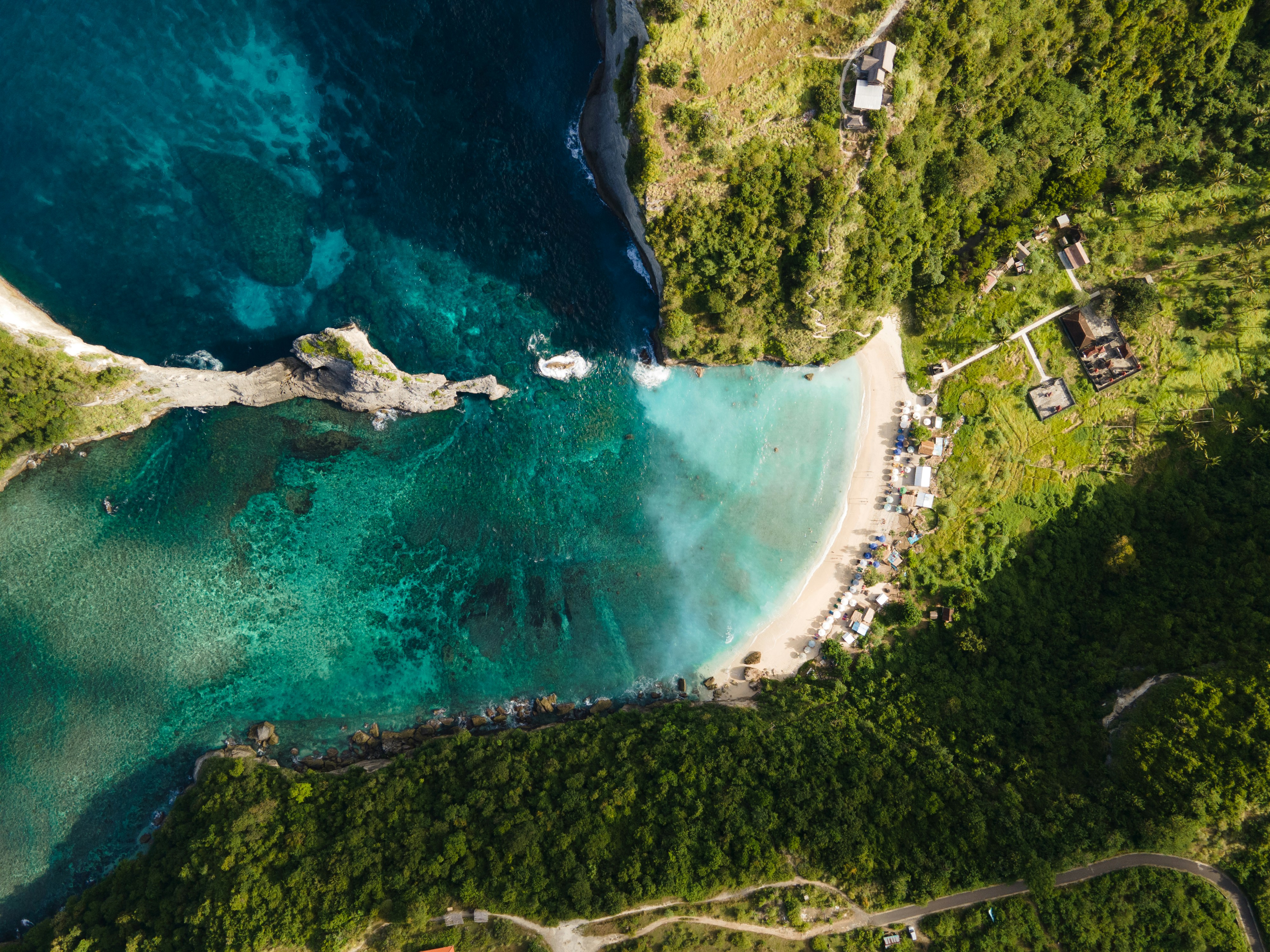 Resa till Bali - Vy ovanifrån på klippor med grönska omgivet av blått hav som möter en strand med hus i Bali