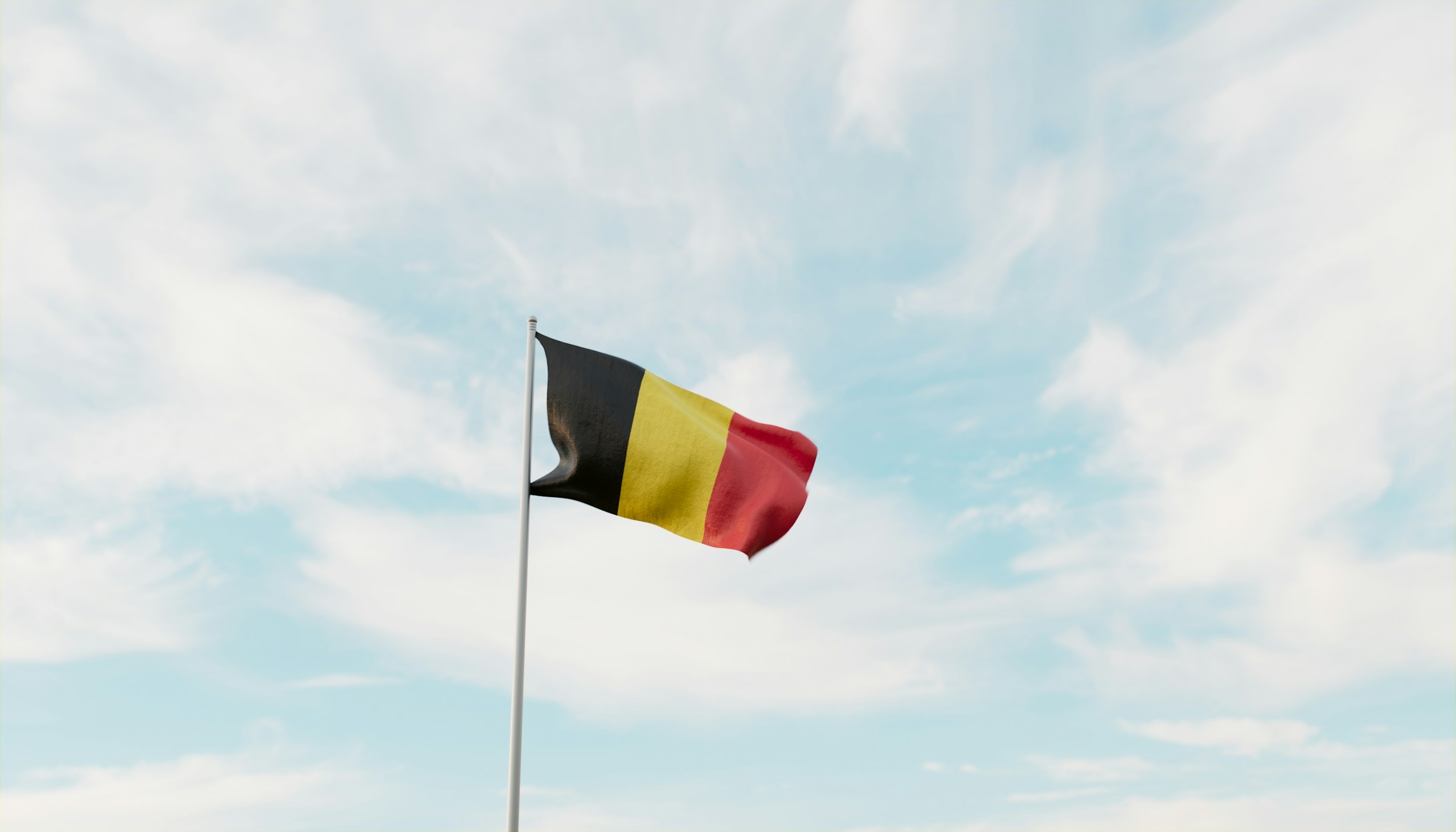 Belgisk flagga vajar mot blå himmel med lätta moln
