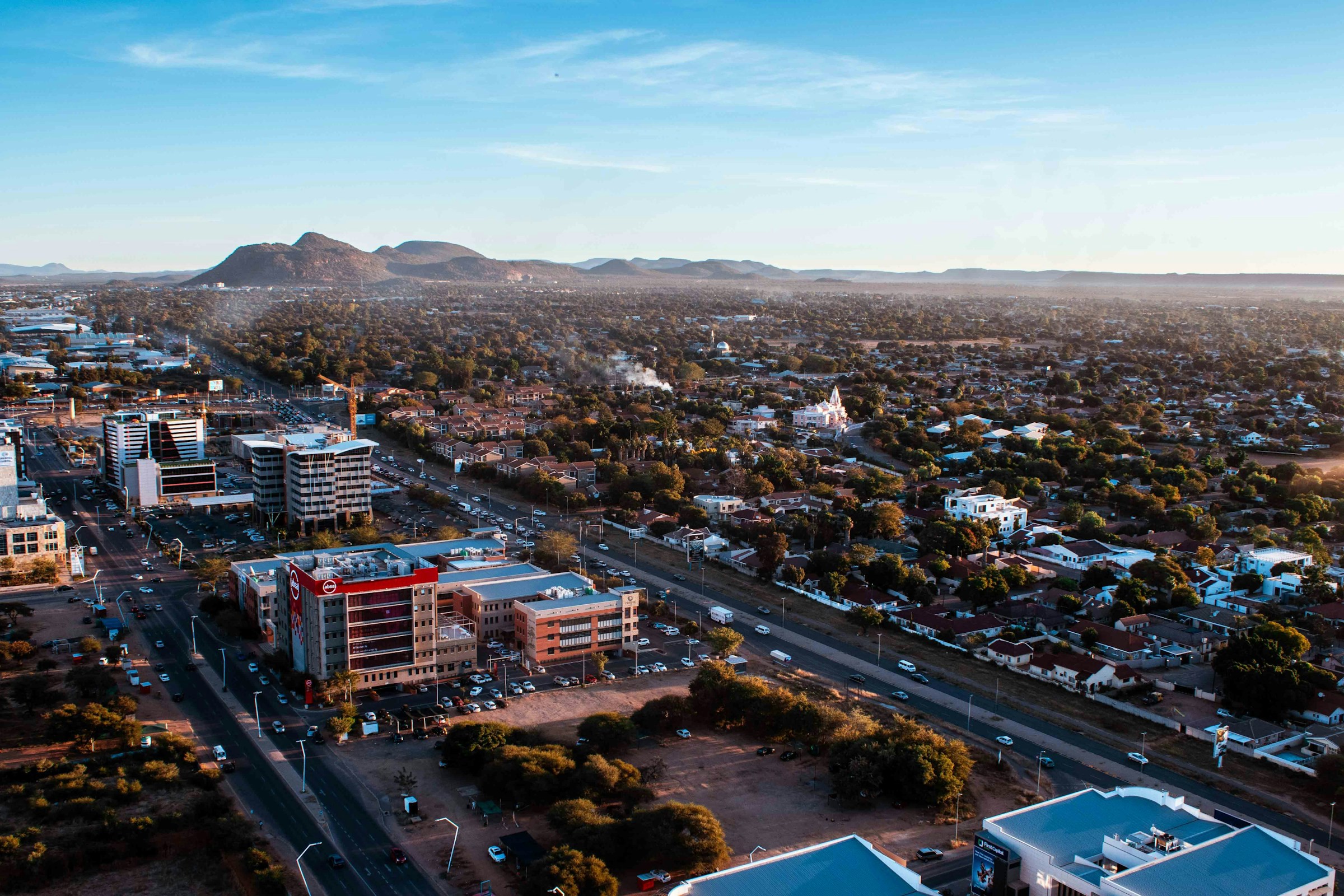 Flygbild över Gaborone, huvudstaden i Botswana vid solnedgång med moderna byggnader och berg i bakgrunden.