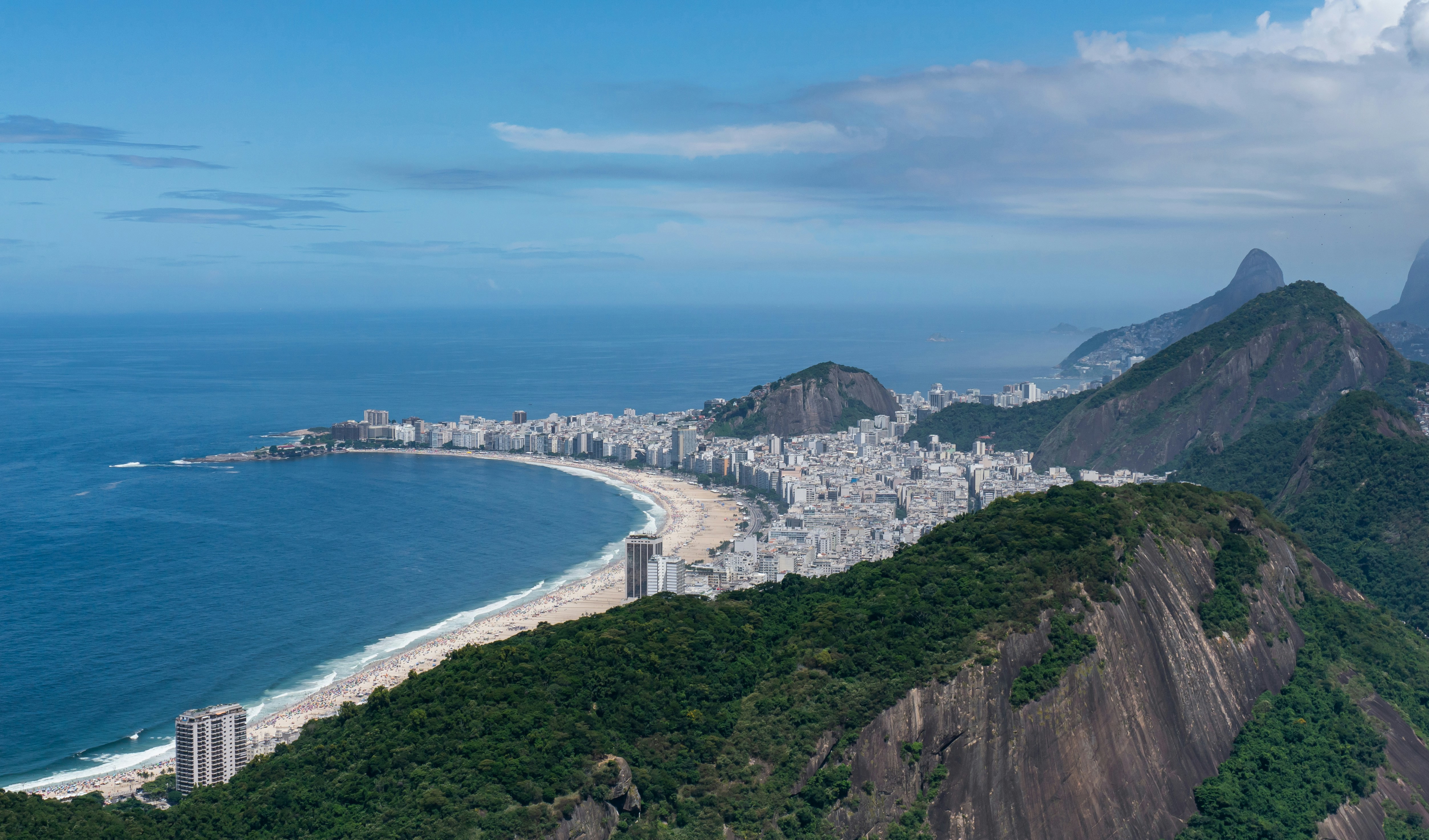 Flygbild över Copacabana-stranden och stadslandskap i Brasilien, med berg och klarblå himmel.