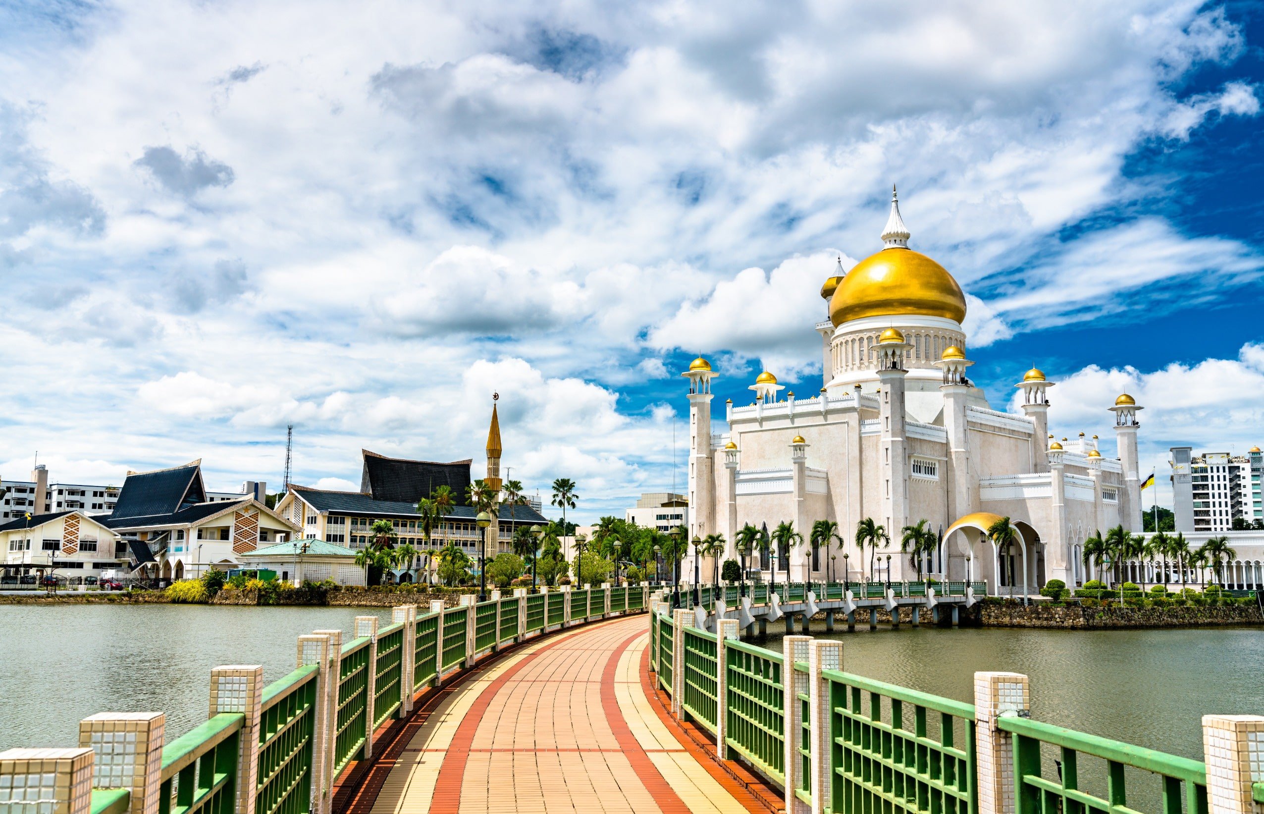 A bridge that leads over a river towards a beautiful white temple with golden towers and blue sky in the background