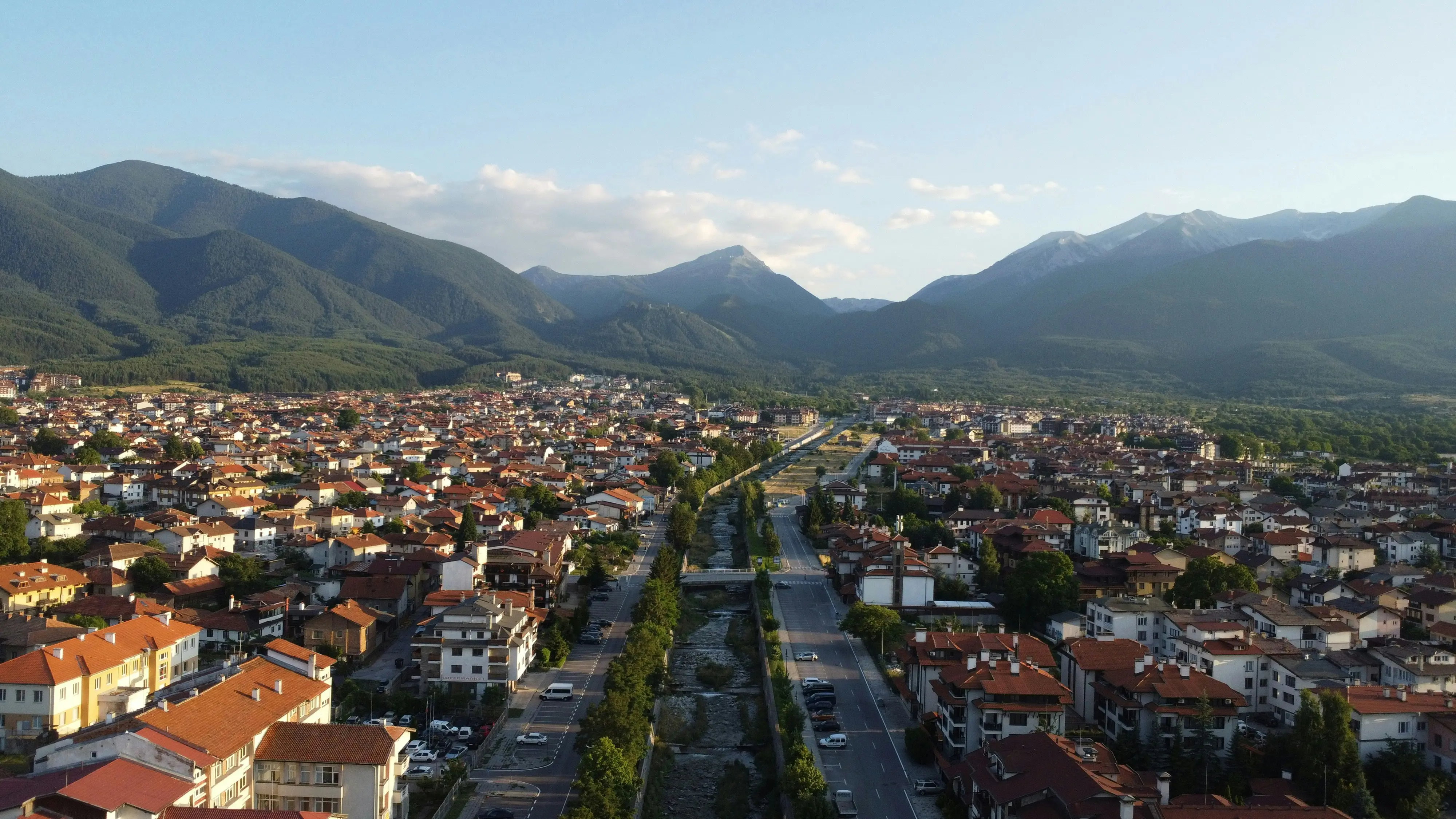 Resa till Bansko - Vy över småstad omgiven av gröna berg och skogar under ljus morgonhimmeI