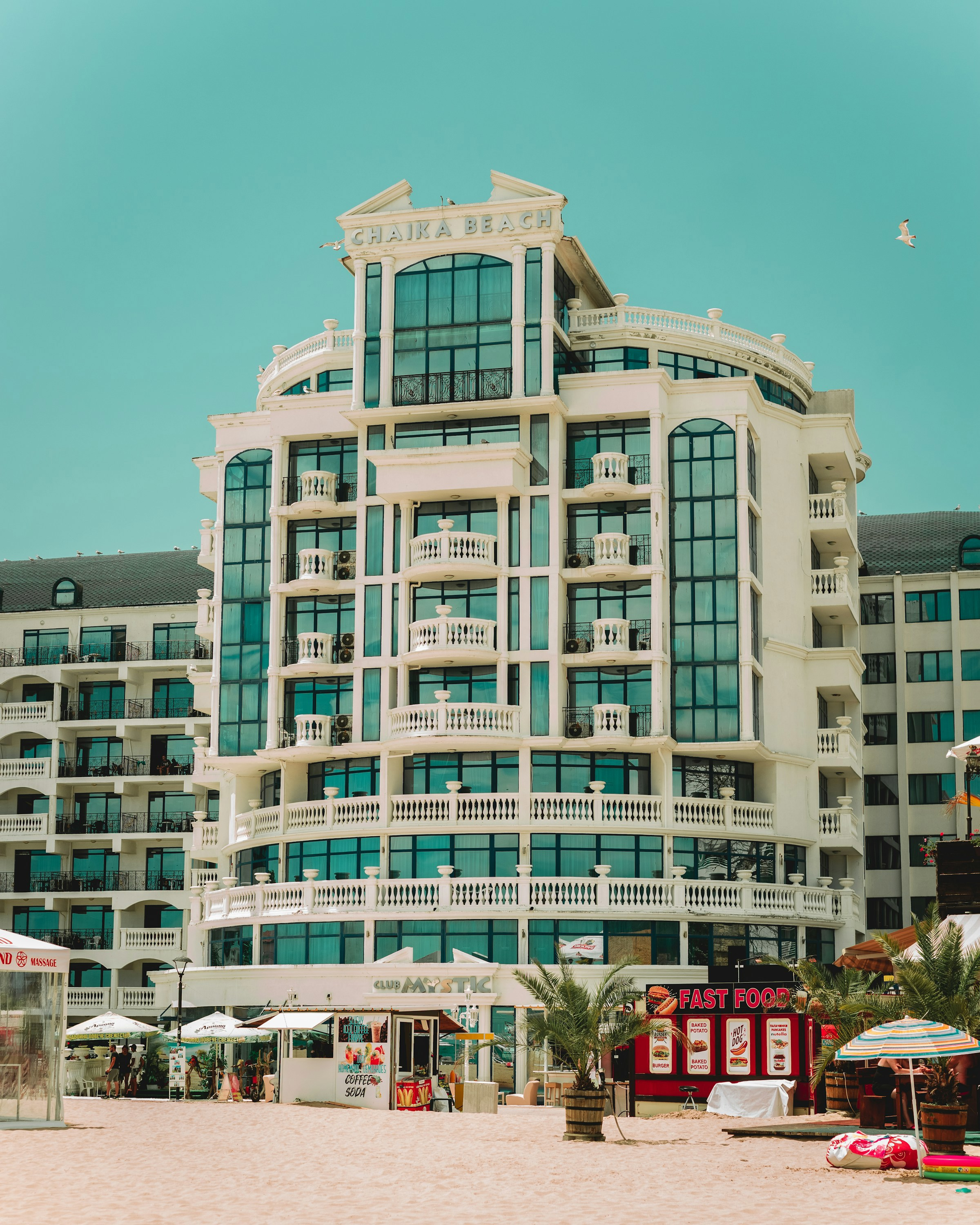 Luxuöst strandhotell med balkonger mot havet, sandstrand med solstolar och snabbmatskiosk framför på en solig dag i Sunny Beach, Bulgarien.