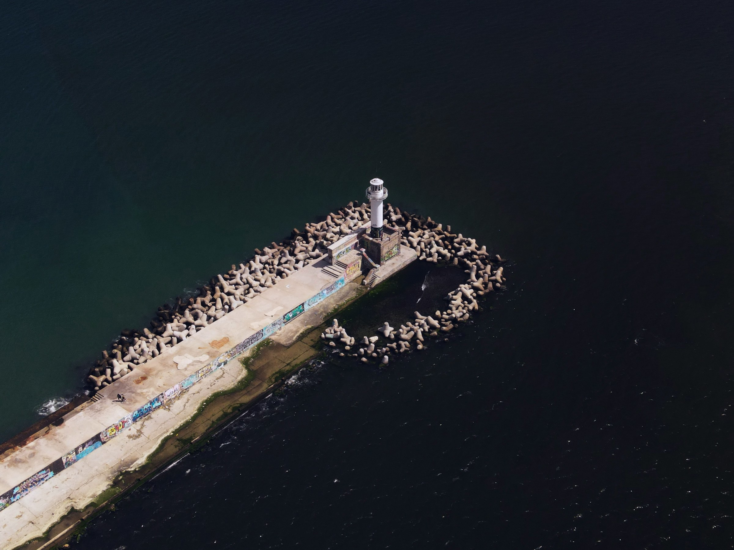 Flygbild av en vit fyrtorn som står på en pir omgiven av bryggelement vid havet i Varna.