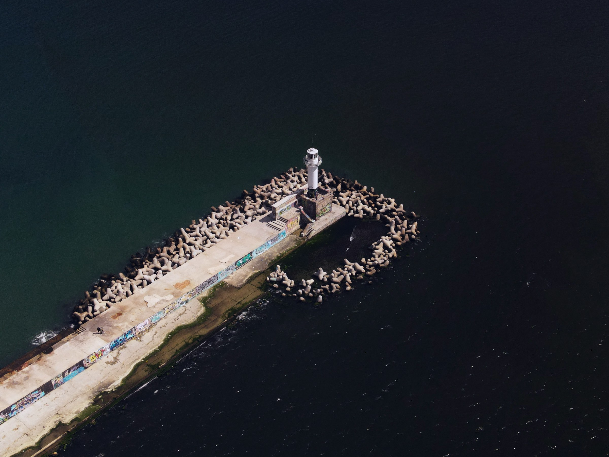 Flygbild av en vit fyrtorn som står på en pir omgiven av bryggelement vid havet i Varna.