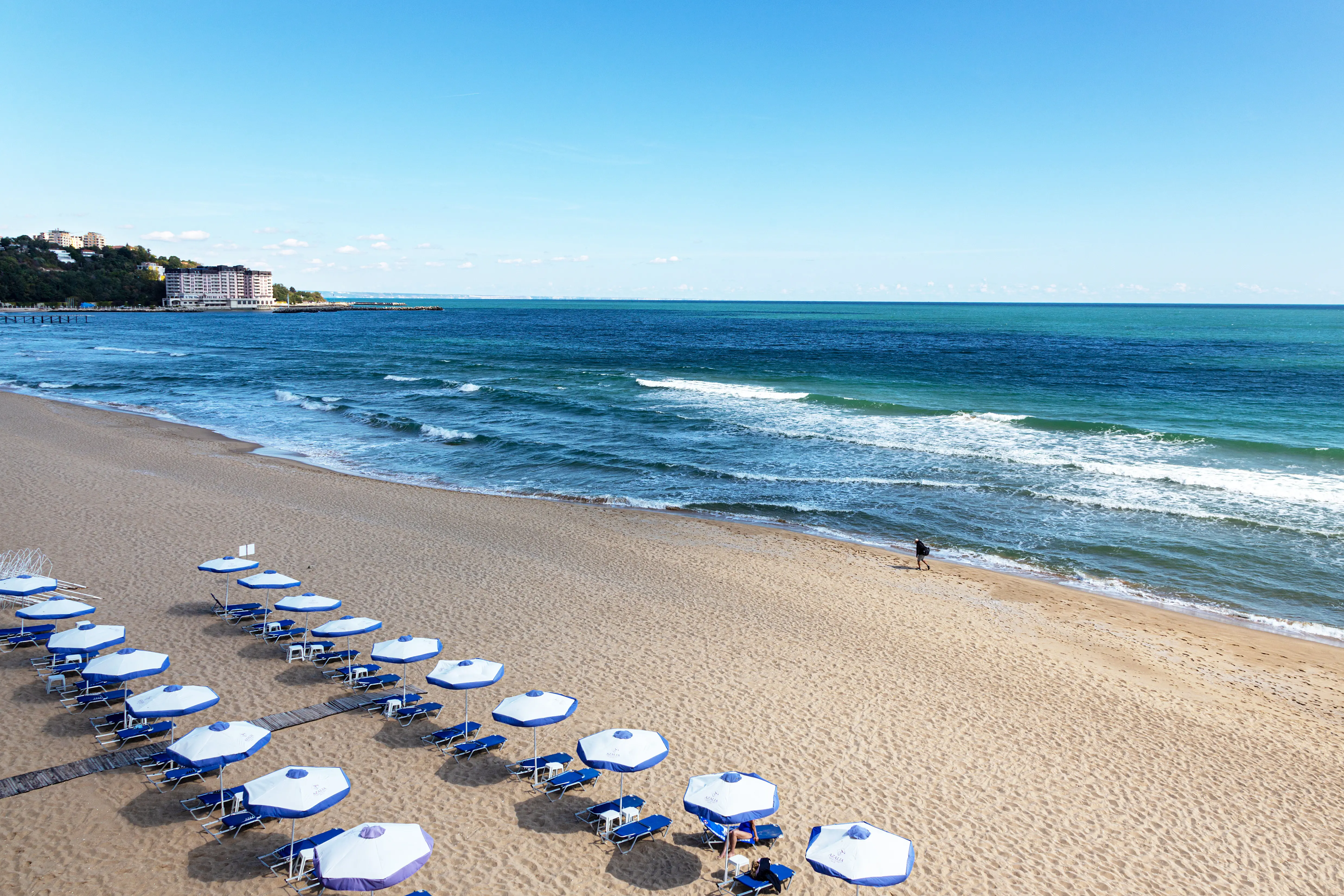 Resa till Sunny Beach - Bulgarien - Havsutsikt över en solig sandstrand med blåa parasoller och vågigt hav.