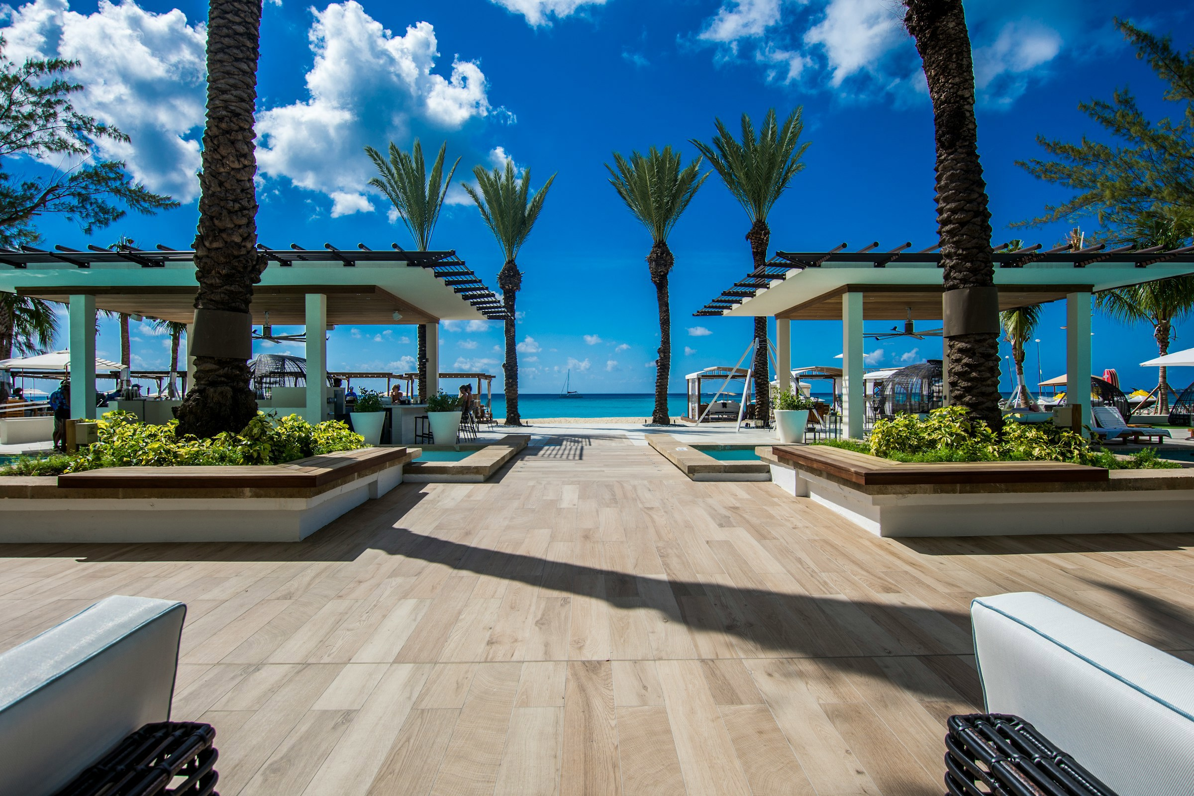 Tropisk strandresort på Caymanöarna med uteservering och solsängar, omgivet av palmer och utsikt över klarblå himmel och hav.
