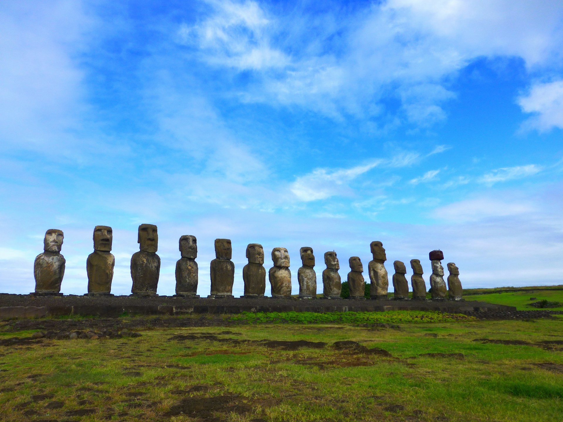 Rad av mystiska moai-statyer på Påskön mot en klarblå himmel och gröna gräsmarker i Chile.