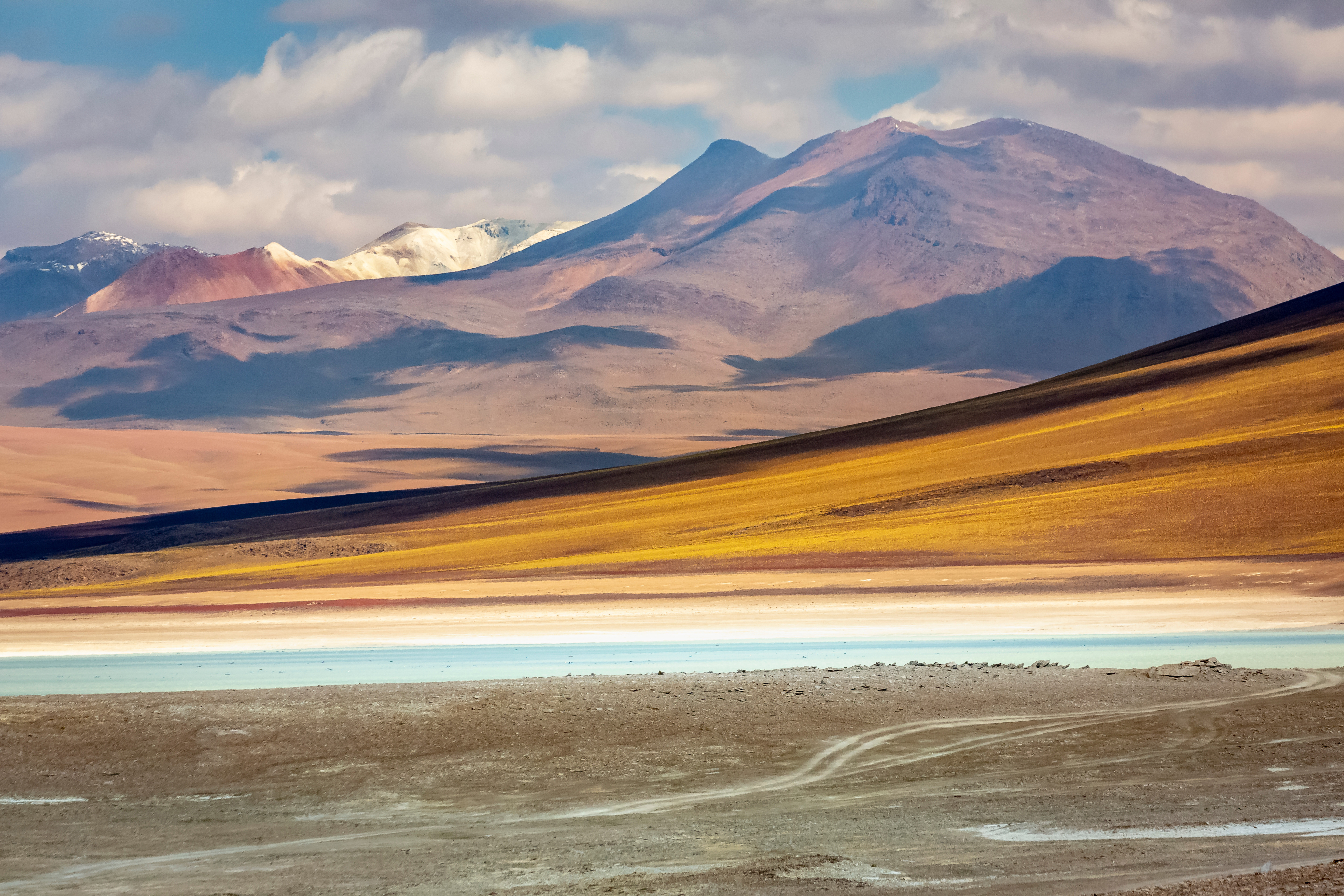 Resa till Chile - Andinskt landskap med mångfärgade kullar och en saltöken framför snötäckta bergstoppar under en klarblå himmel.