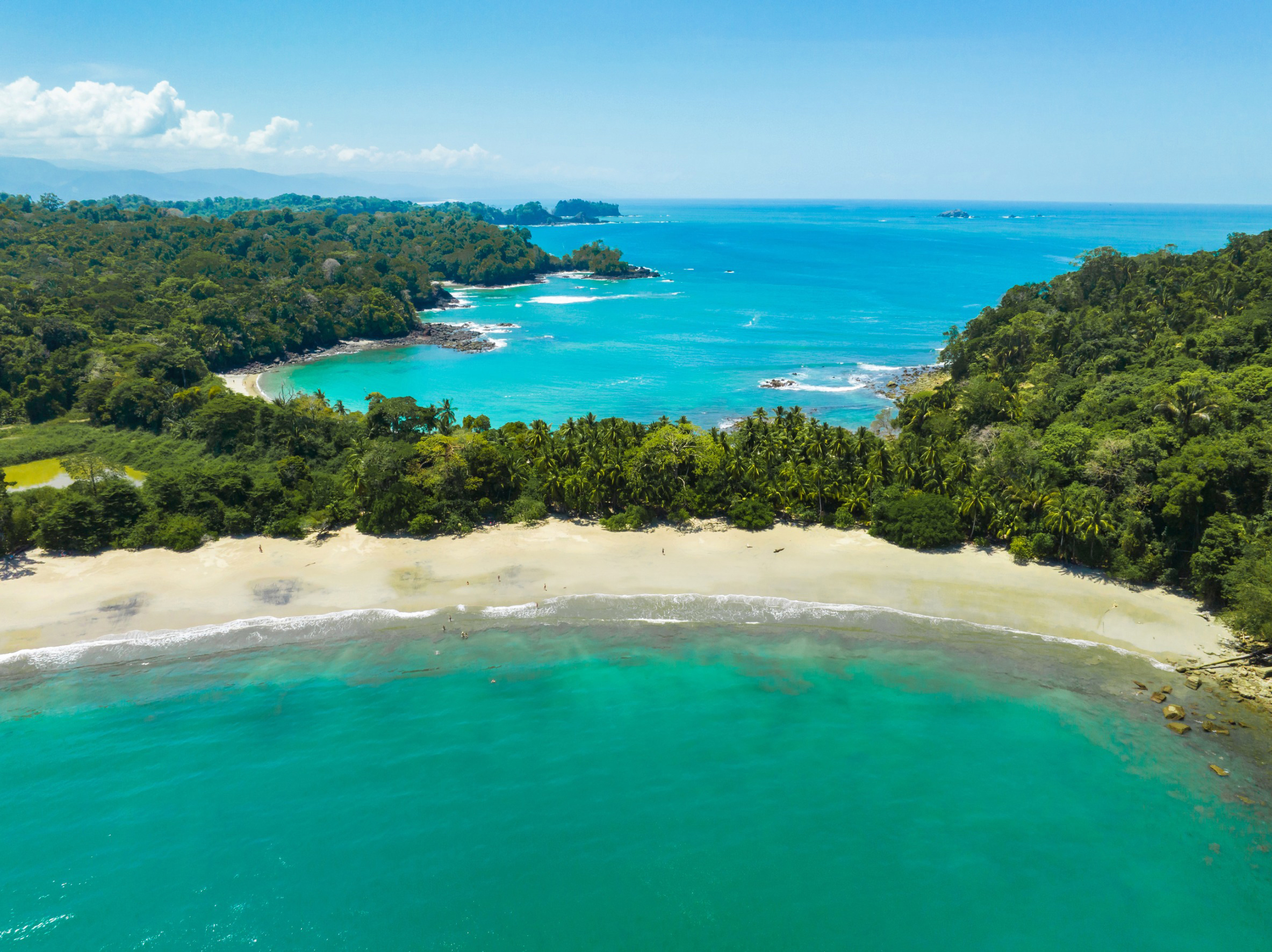 Resa till Costa Rica - Flygbild av en tropisk strand med kristallklart vatten och frodig grönska i kustnära landskap.