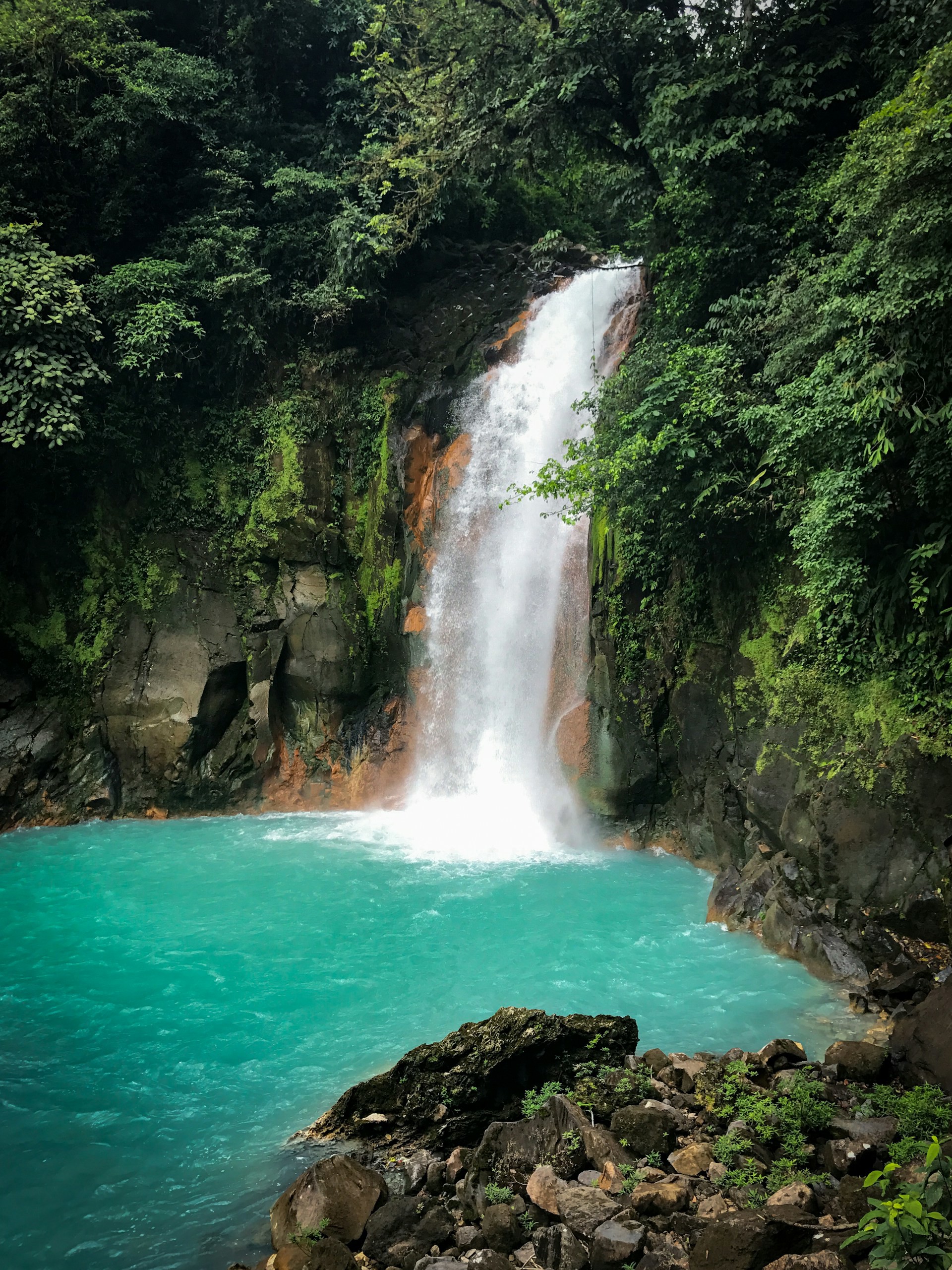 Turkosblått vatten i en tropisk vattenfall omgiven av frodig grönska och klippor i Costa Rica.