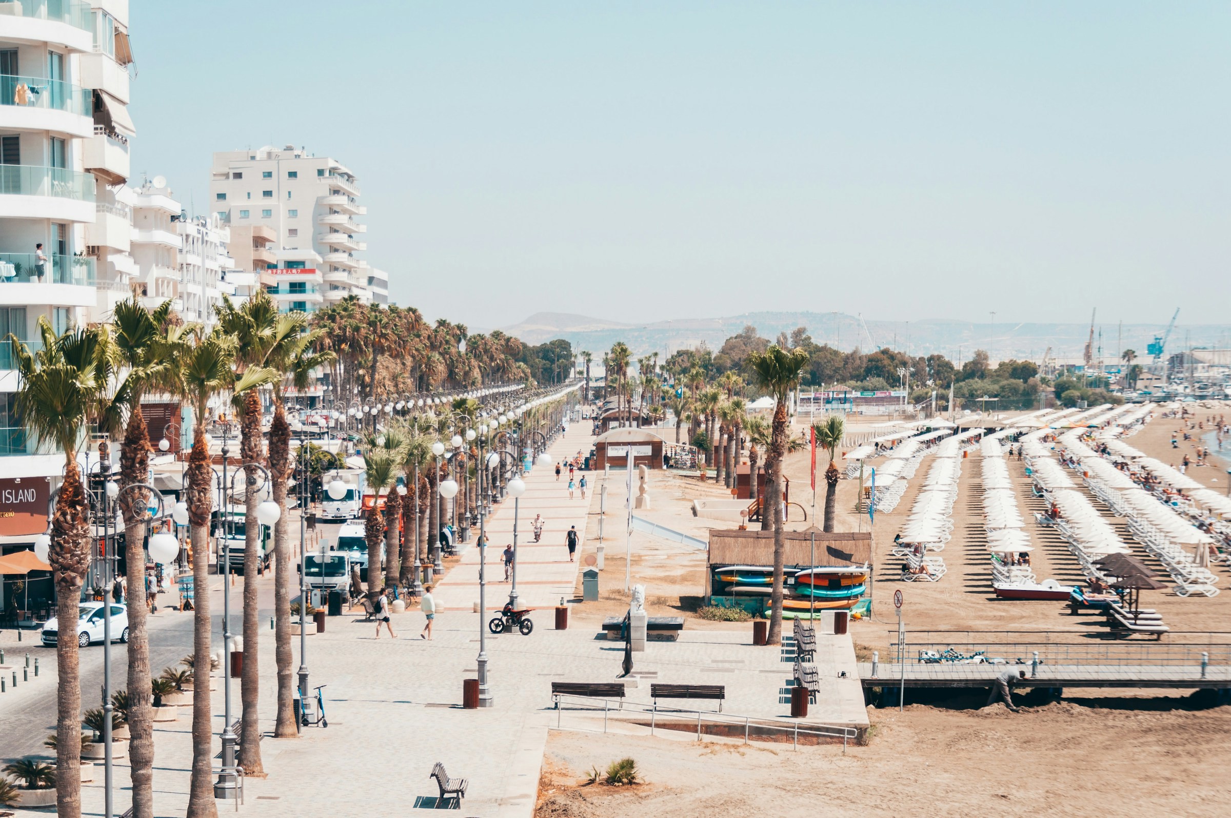 Livlig strandpromenad med palmer och uteserveringar i ett soligt Larnaca.