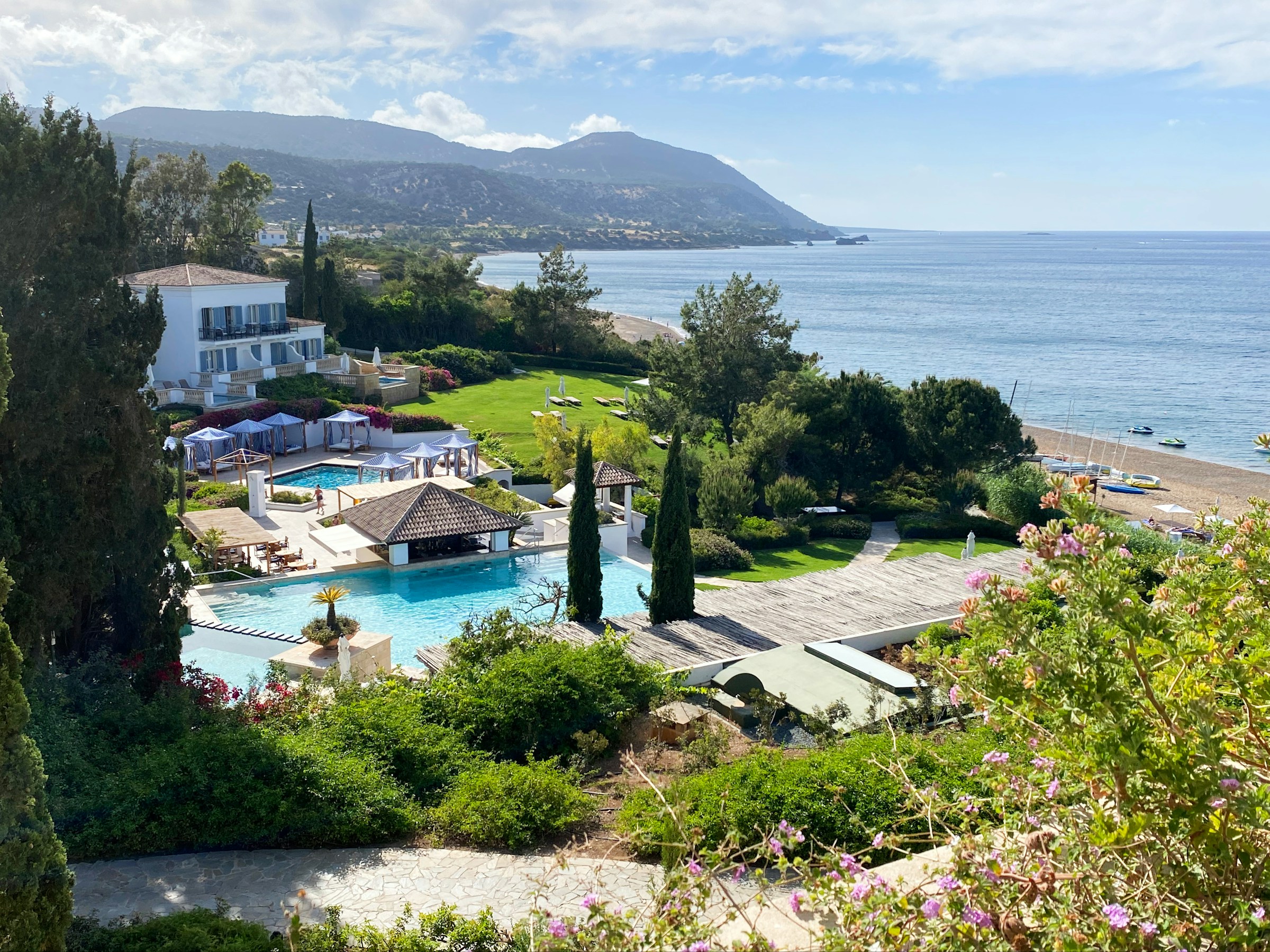 Lyxigt semesterort vid havet med pool och trädgård, med utsikt över berg och klarblå himmel på Cypern.