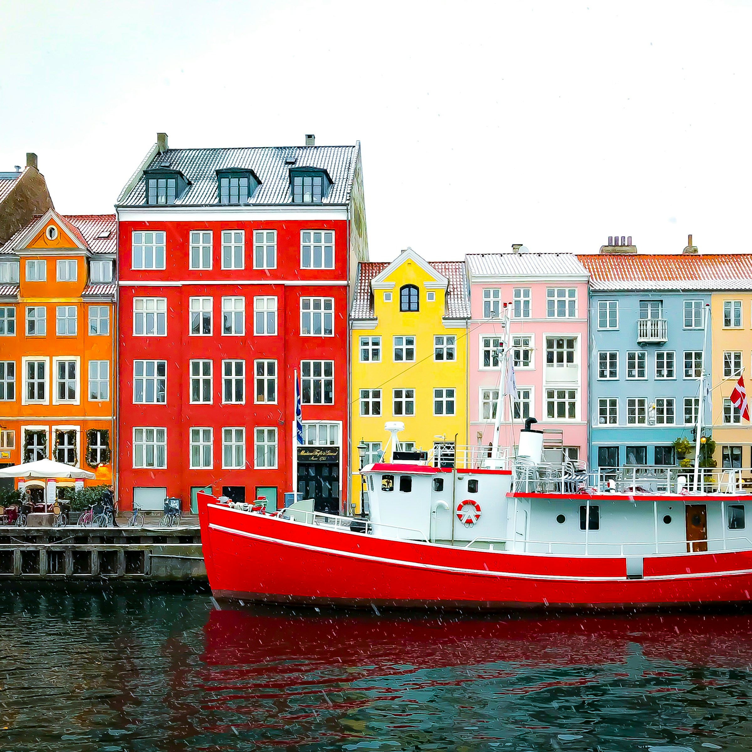 Färgglada traditionella skandinaviska byggnader vid hamnen med röd båt i förgrunden i Köpenhamn.