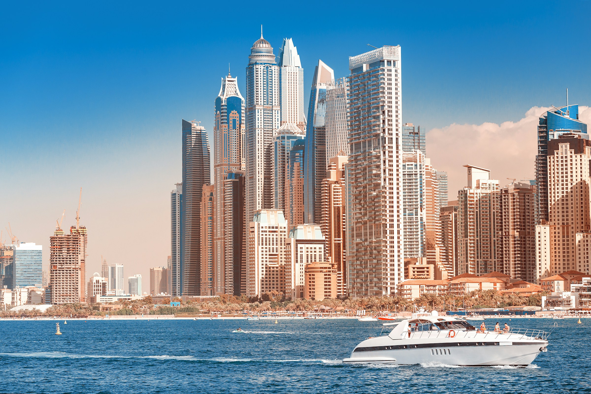 Motorbåt med passagerare framför en imponerande stadssilhuett med moderna skyskrapor och blå himmel i Dubai.