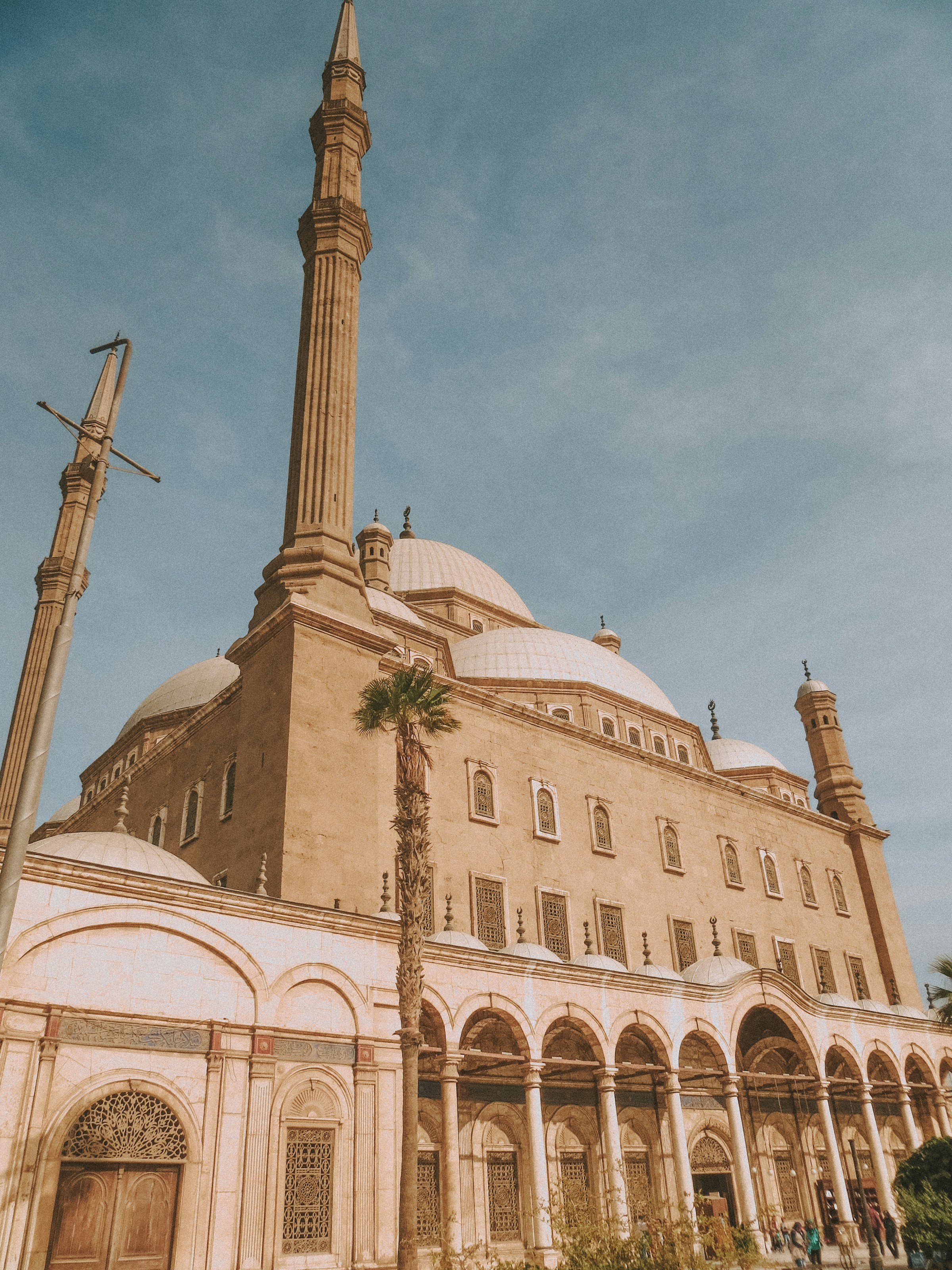 Imponerande moské med kupol och minareter i Kairo mot en klarblå himmel i dagsljus, arkitektoniska detaljer och besökare i förgrunden.