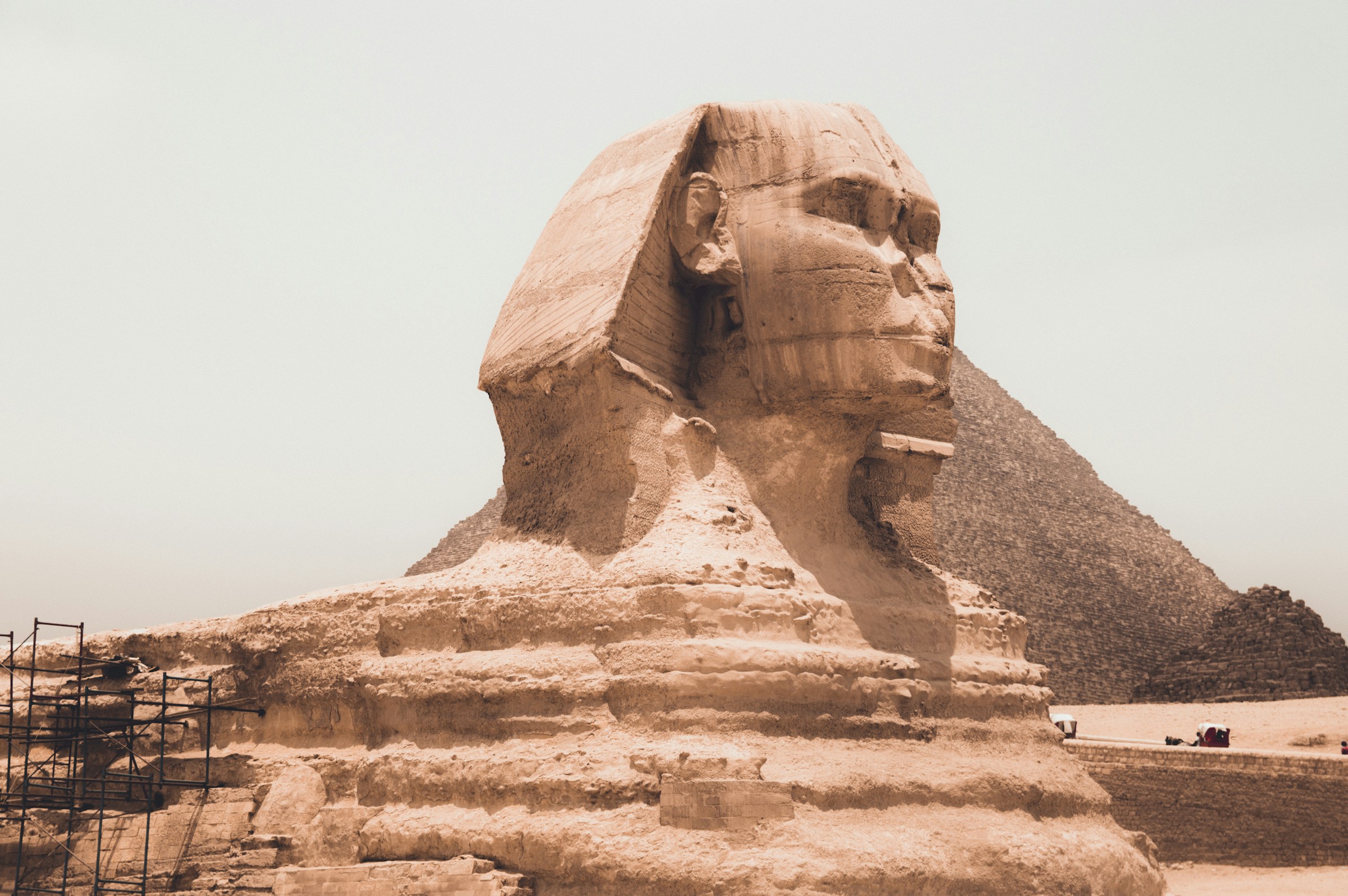 Sfinksen i Giza under grå himmel med pyramid i bakgrunden, ett historiskt monument i Egypten.
