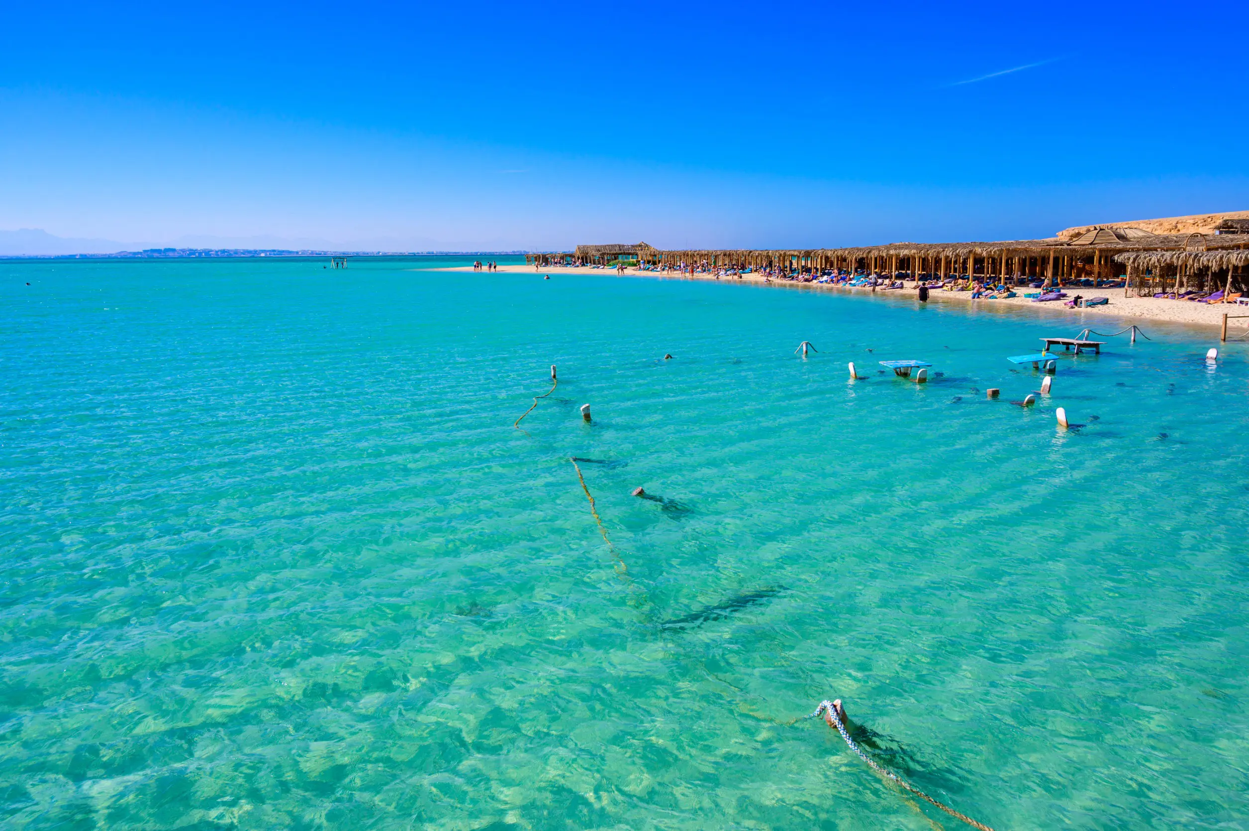 Resa till Hurghada - Klart turkost vatten vid en solig semesterort med strandparasoller och badgäster i Hurghada.