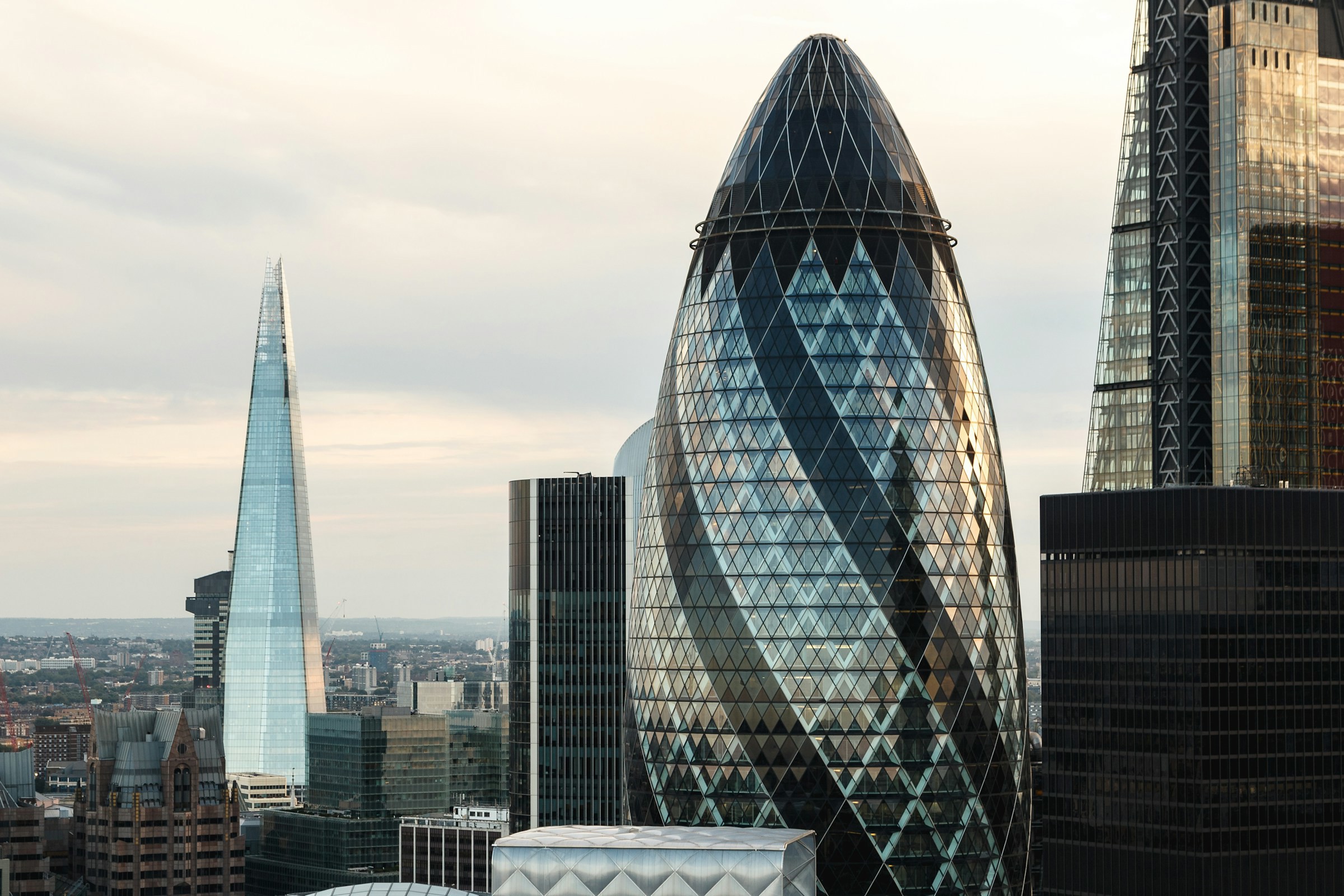 Panoramavy över Londons stadssilhuett med den ikoniska skyskrapan The Shard och Gherkin-byggnaden i förgrunden vid skymningen.