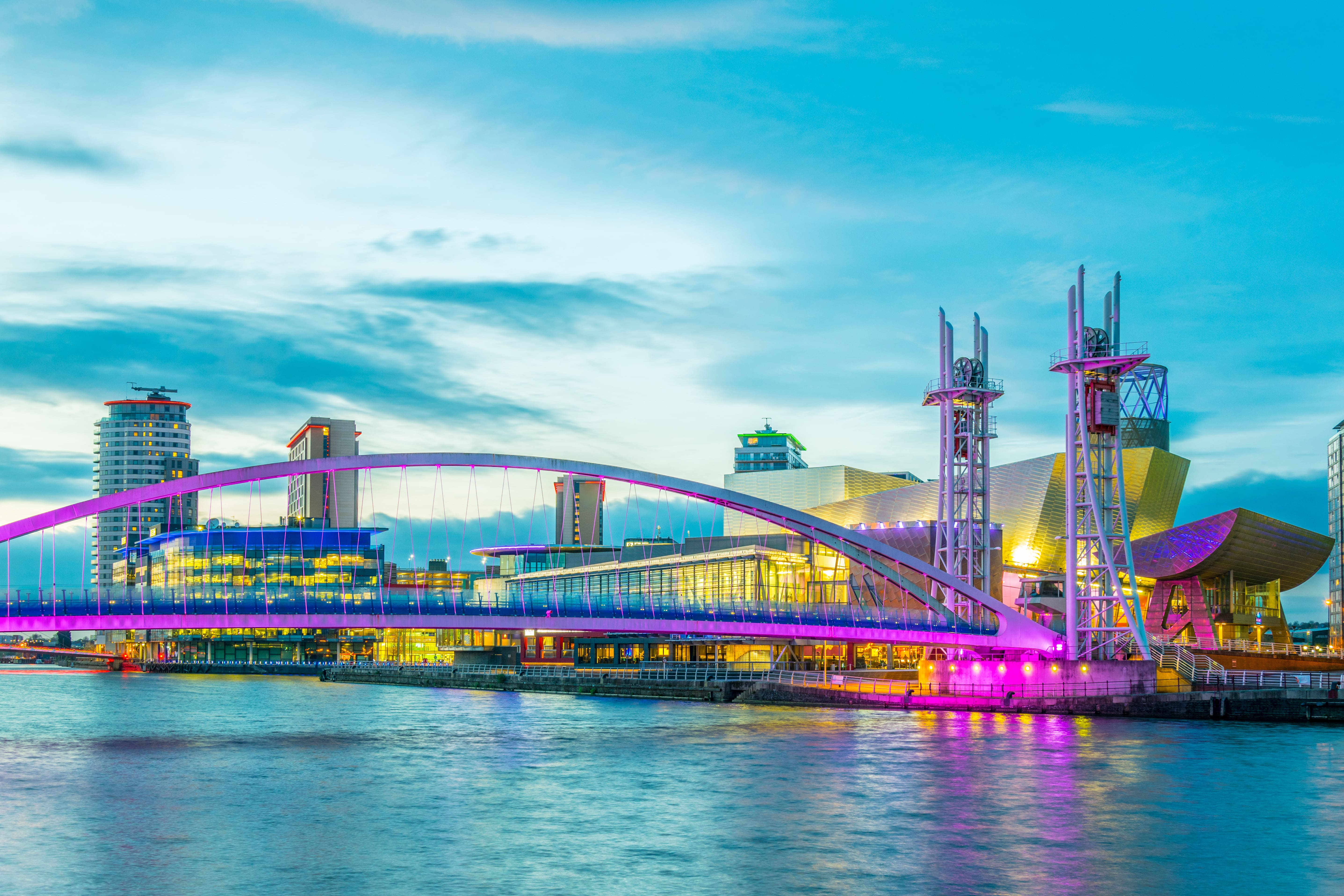 Travel to Manchester - View of a river with Manchester city and towers in the background during early sunset