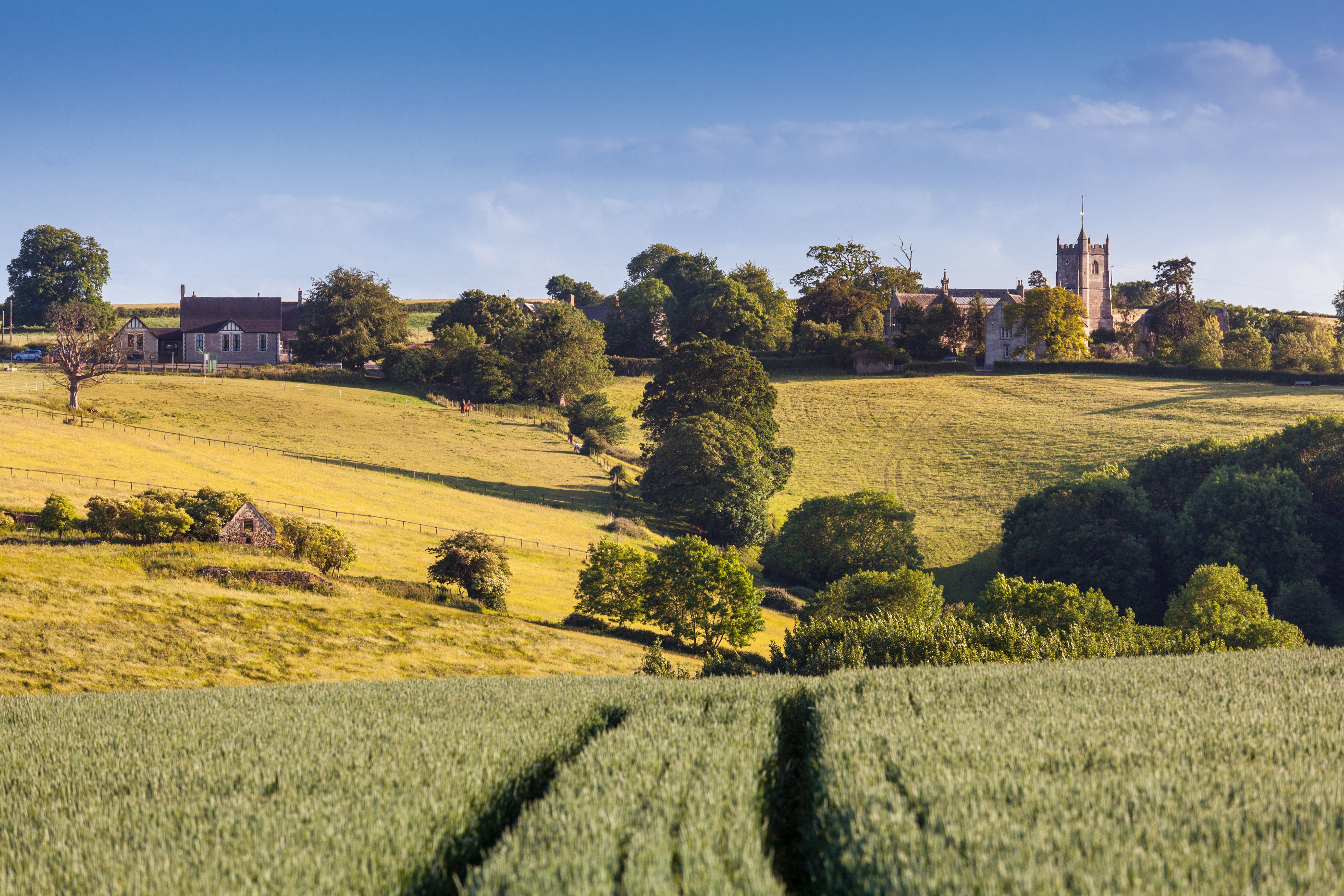 Resa till England - Idylliskt landskap med kyrka och bondgårdar i det brittiska landsbygden, gröna fält och blå himmel.
