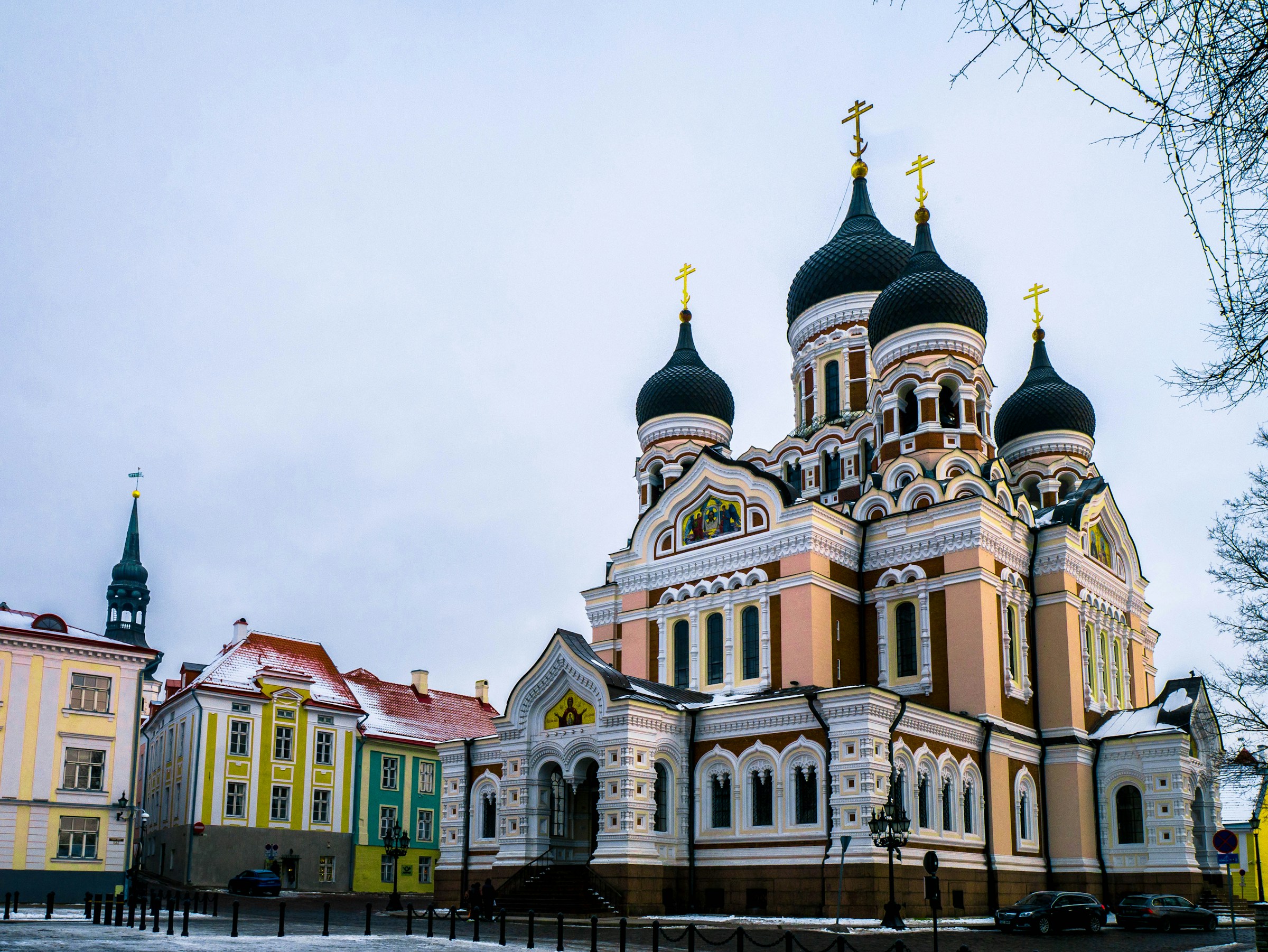 Färgstarka Alexander Nevskij-katedralen i Tallinn med traditionella byggnader i förgrunden på en molnig dag.