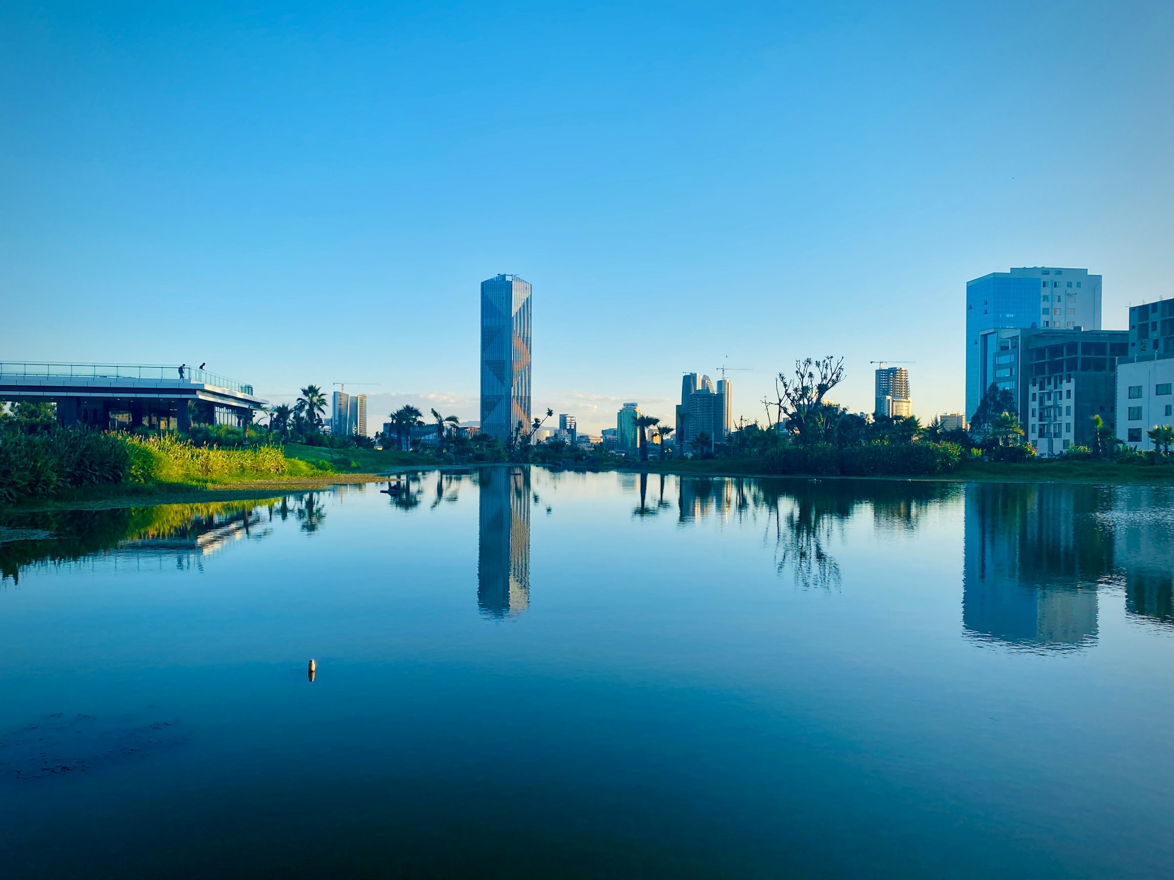 Stadssilhuett reflekterad i stilla vatten vid solnedgång med moderna byggnader och frodig vegetation i Addis Ababa, Etiopien.