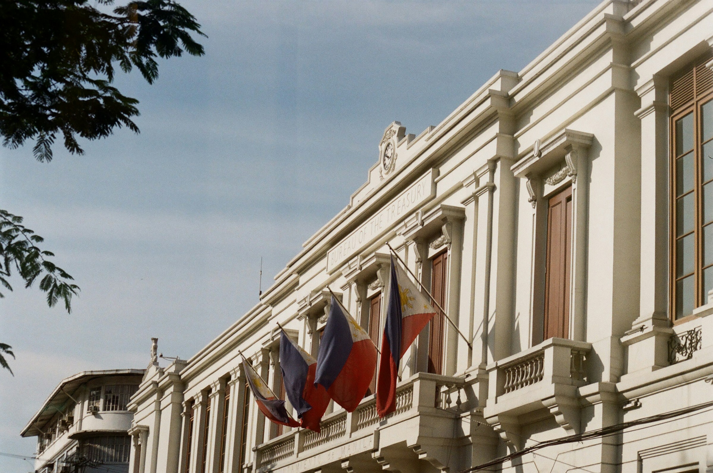 Klassisk vit byggnad med skylt som säger 'BUREAU OF THE TREASURY' och flaggor som fladdrar i vinde i Manilla.
