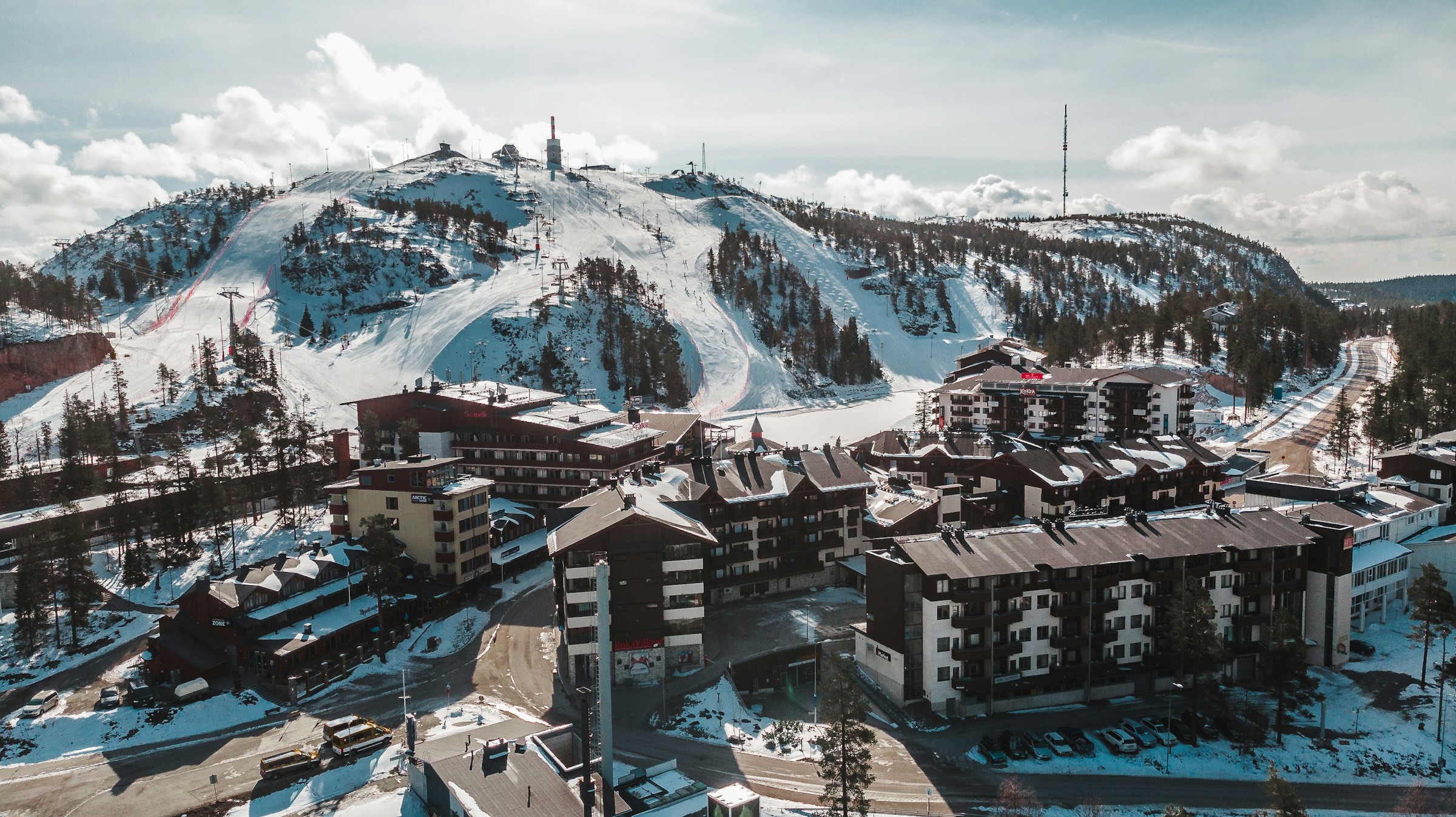 Vy över skidbacke i Ruka, Finland som leder ner till ett resort och byggnader, allt täckt i snö