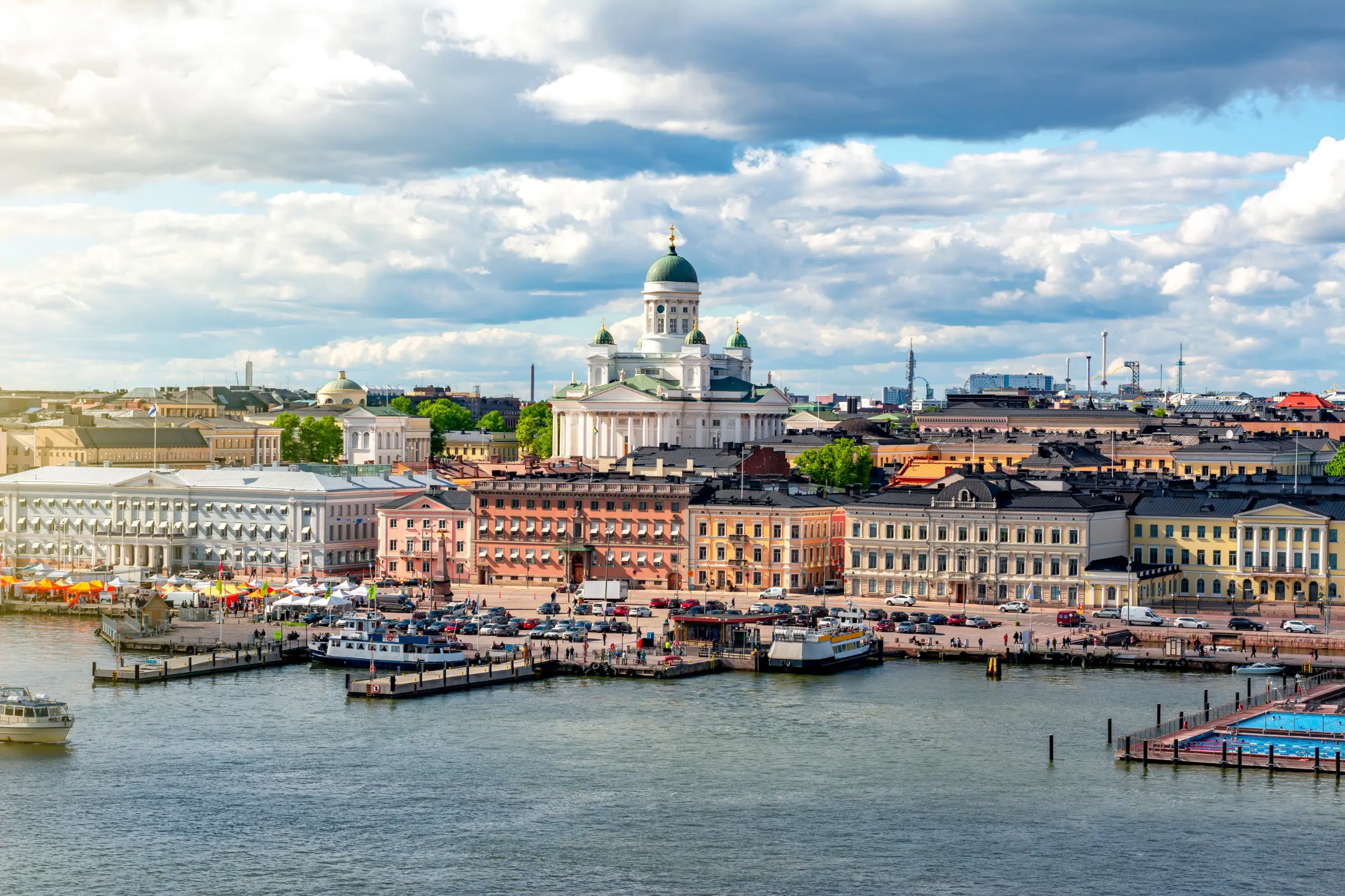 Resa till Helsingfors - Vy över Helsingfors hamn med salutorget, färgglada byggnader och Helsingfors domkyrka, en solig dag.