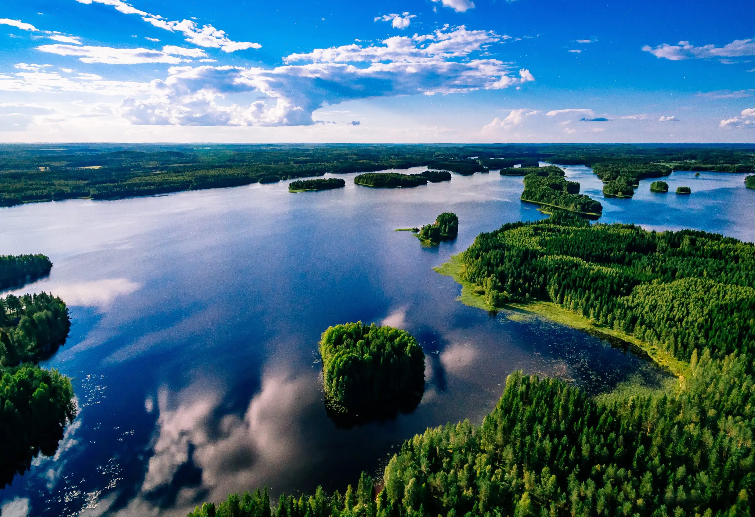 Resa till Finland - Luftvy av en spegelblank sjö med skogsbeklädda öar under blå himmel i Finland.