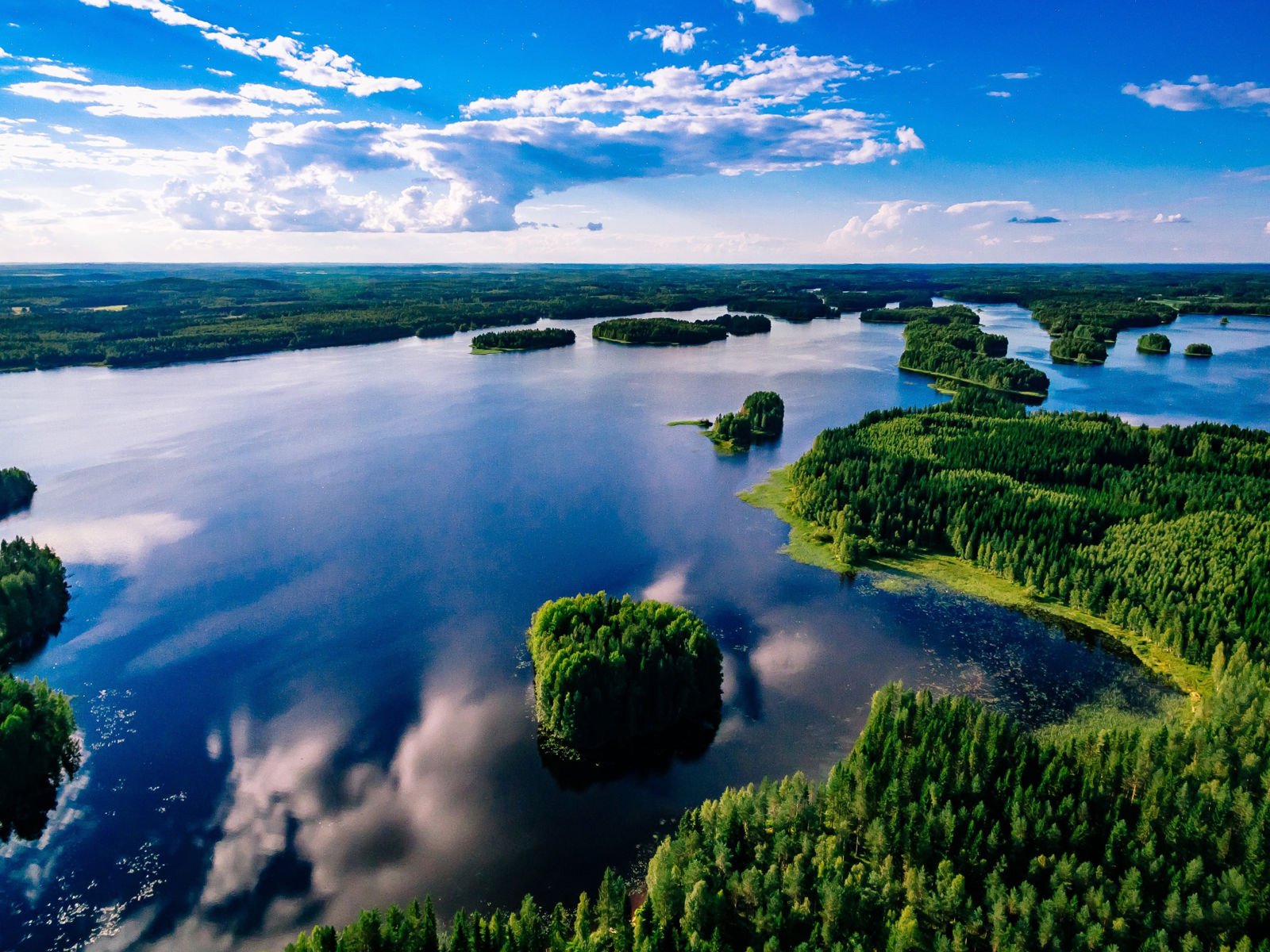 Resa till Finland - Luftvy av en spegelblank sjö med skogsbeklädda öar under blå himmel i Finland.