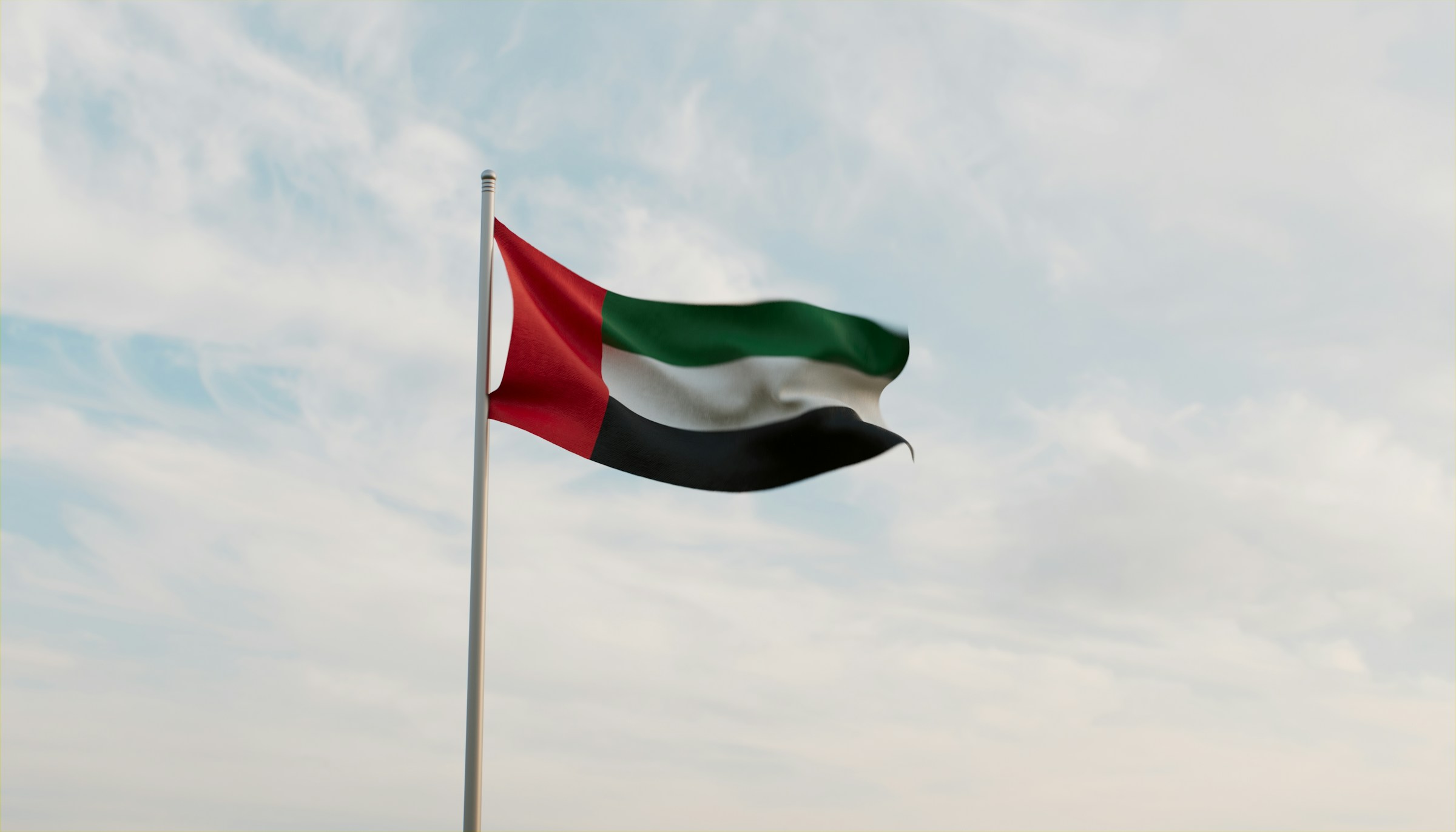 Flagga av Förenade Arabemiraten vajar mot en klar himmel.